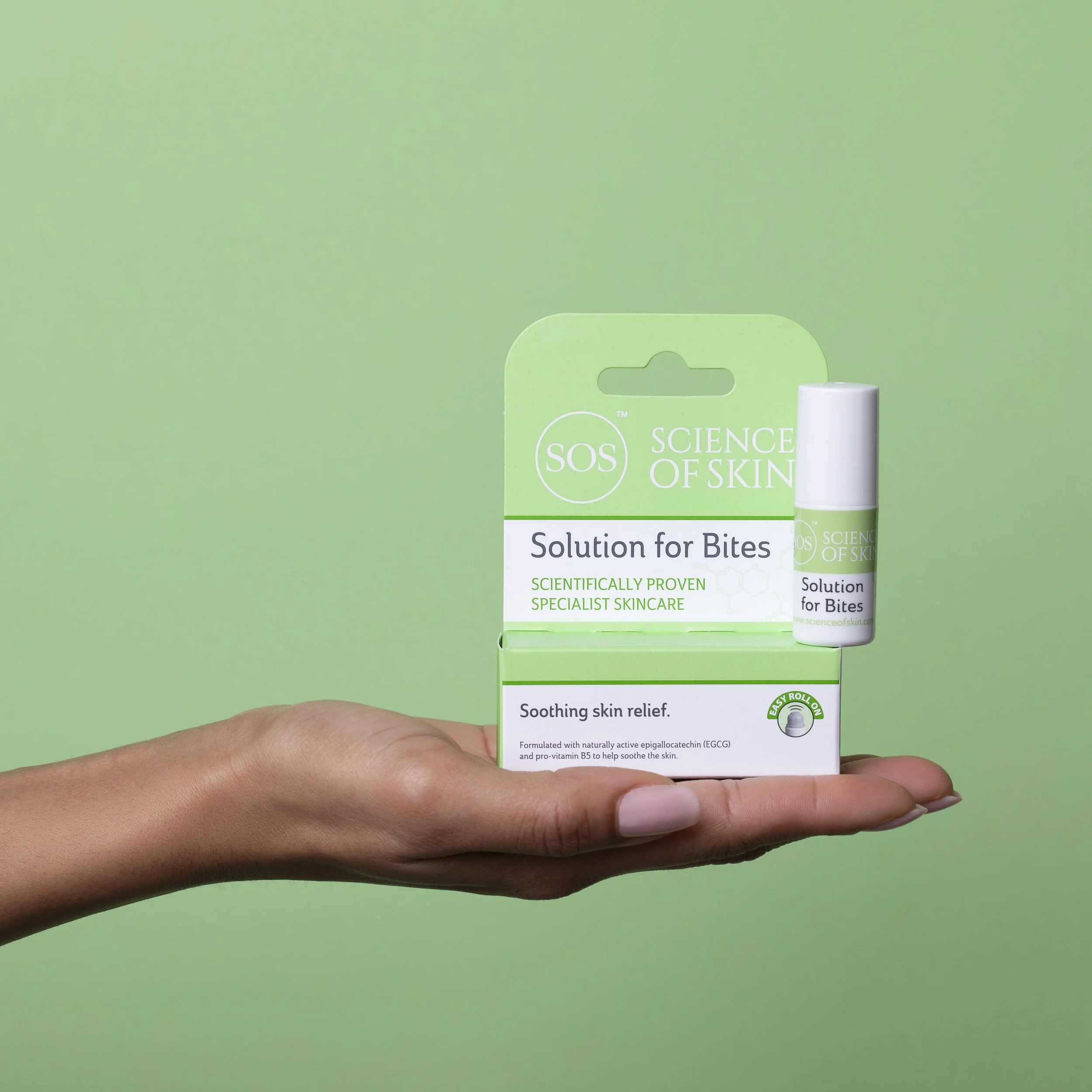 Skincare Product photography A hand holding a box of Science of Skin Solution for Bites against a green background.