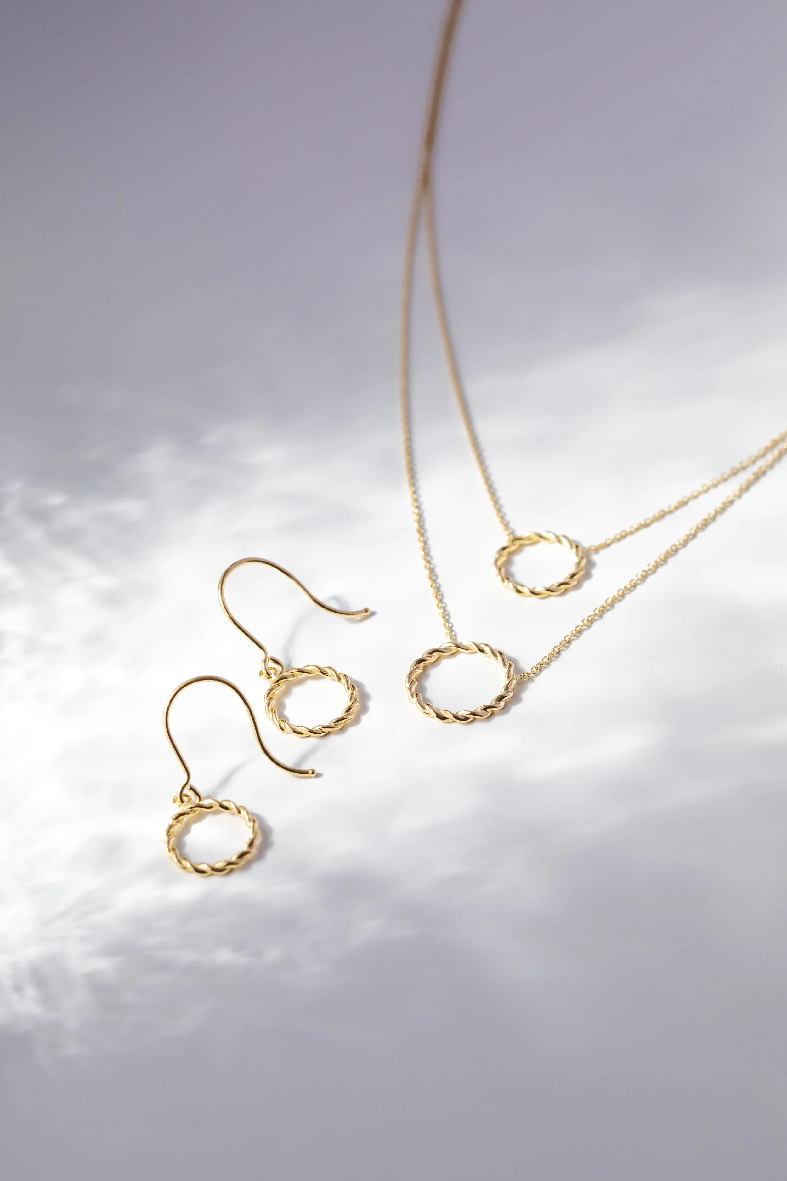 Gold jewelry set, including a necklace and matching earrings with twisted circular designs, displayed on a reflective surface.