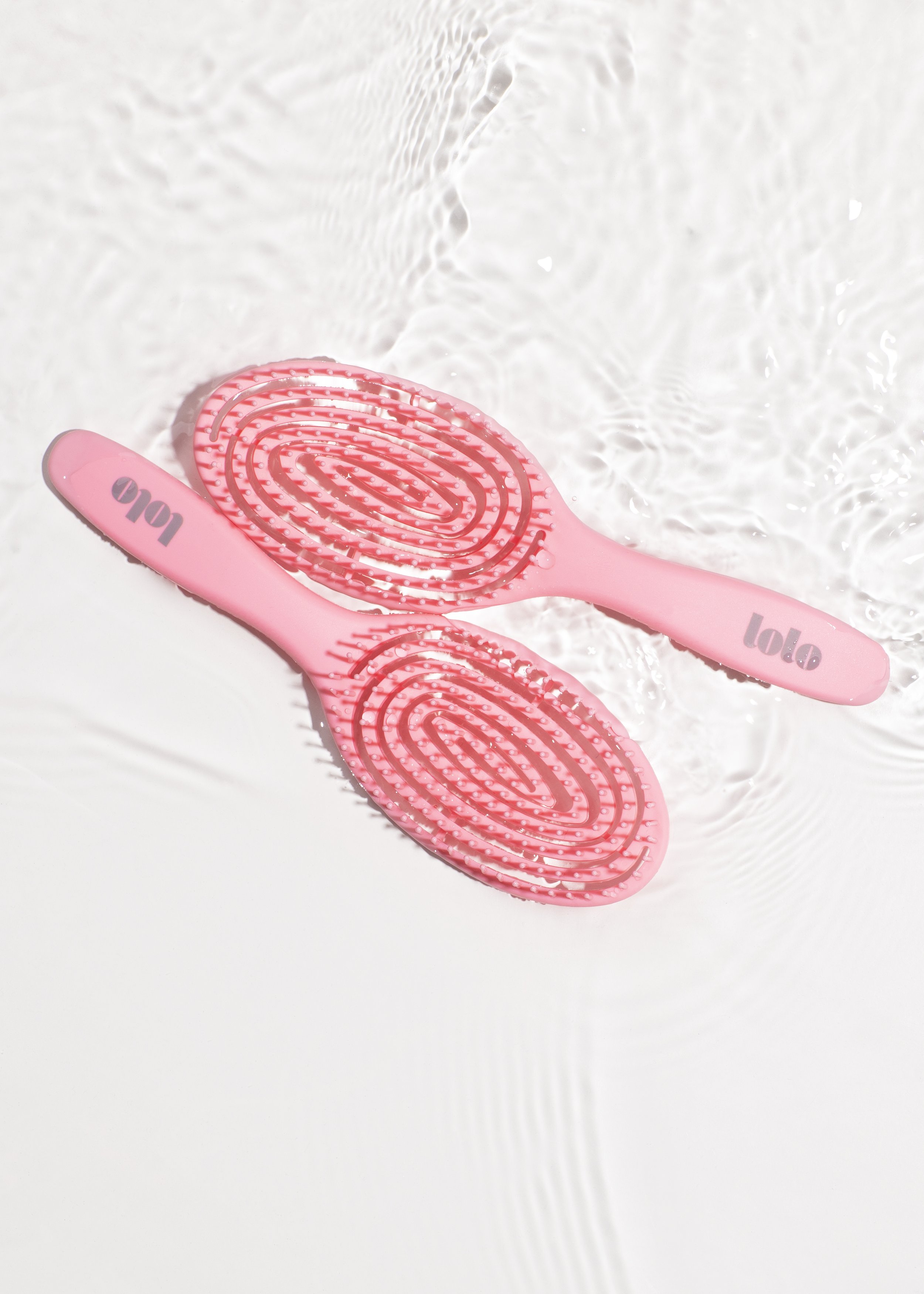 Pink silicone massage slippers with textured soles, floating on water with ripple effects.