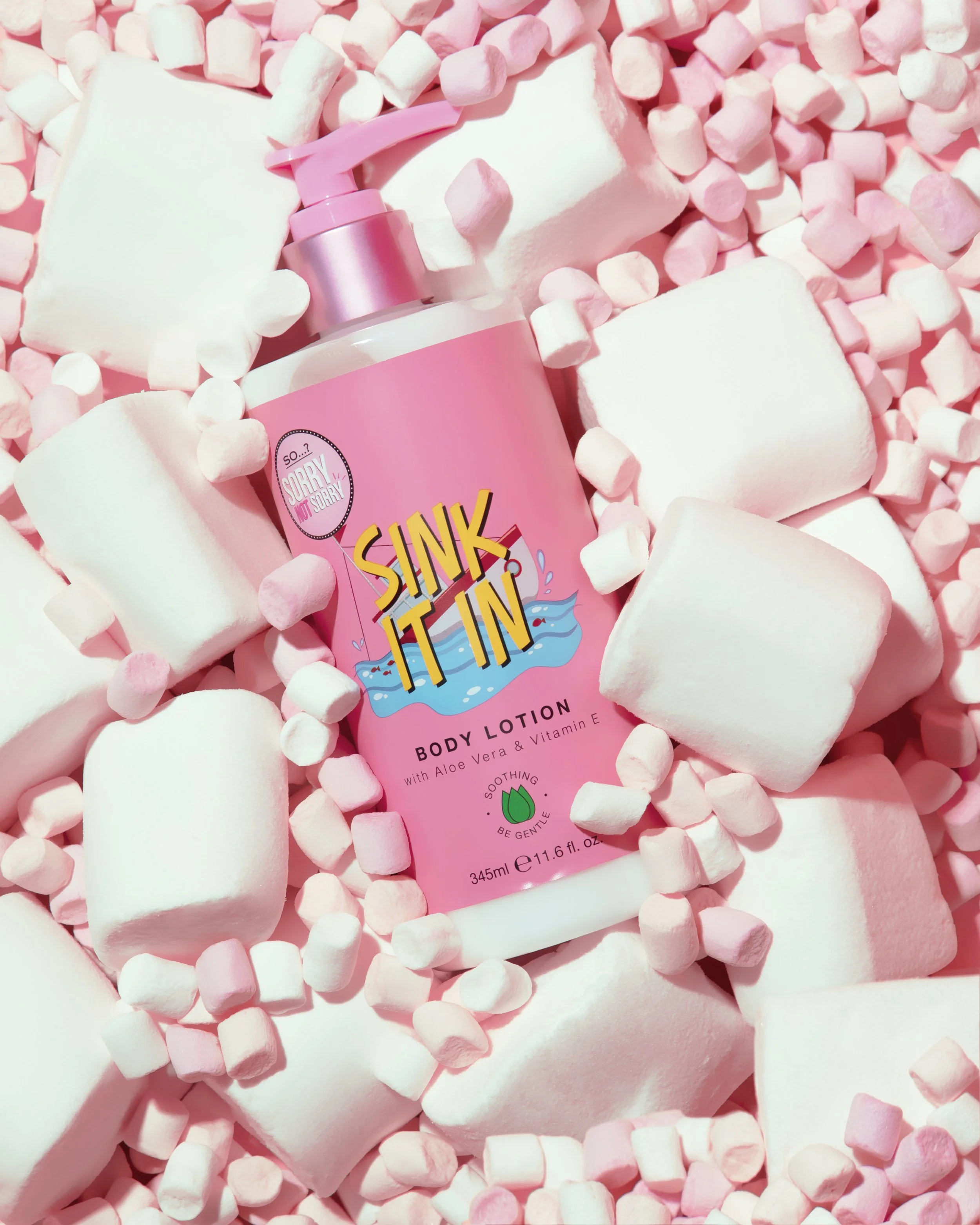 Pink body lotion bottle labeled "Sink It In" surrounded by pink marshmallows and small marshmallow pieces.