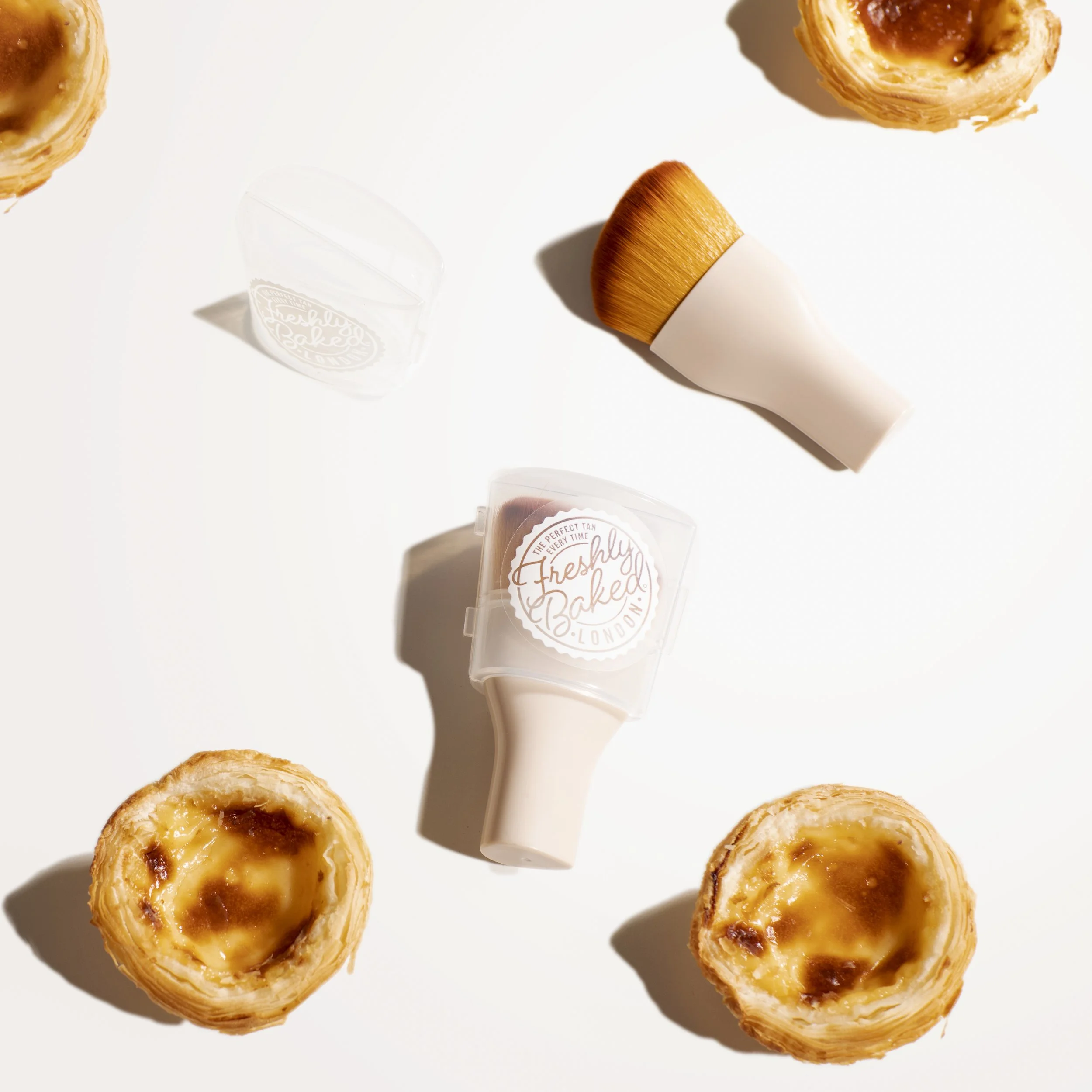 A flat lay of two Portuguese egg tarts and two Freshly Baked skincare brushes on a white background.