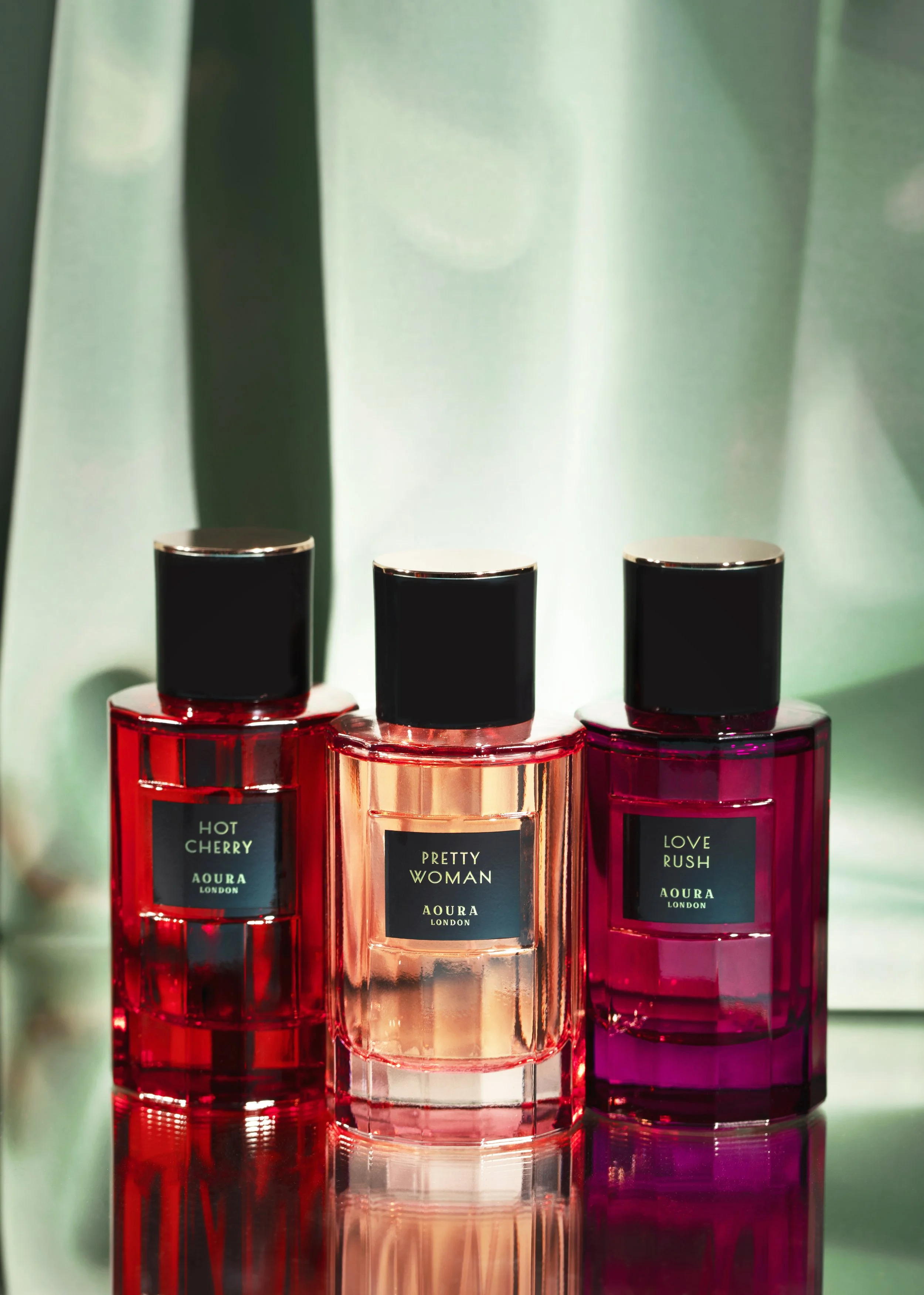 Three bottles of perfume with black caps and black labels, labeled 'Hot Cherry,' 'Pretty Woman,' and 'Love Rush,' against a light green background.