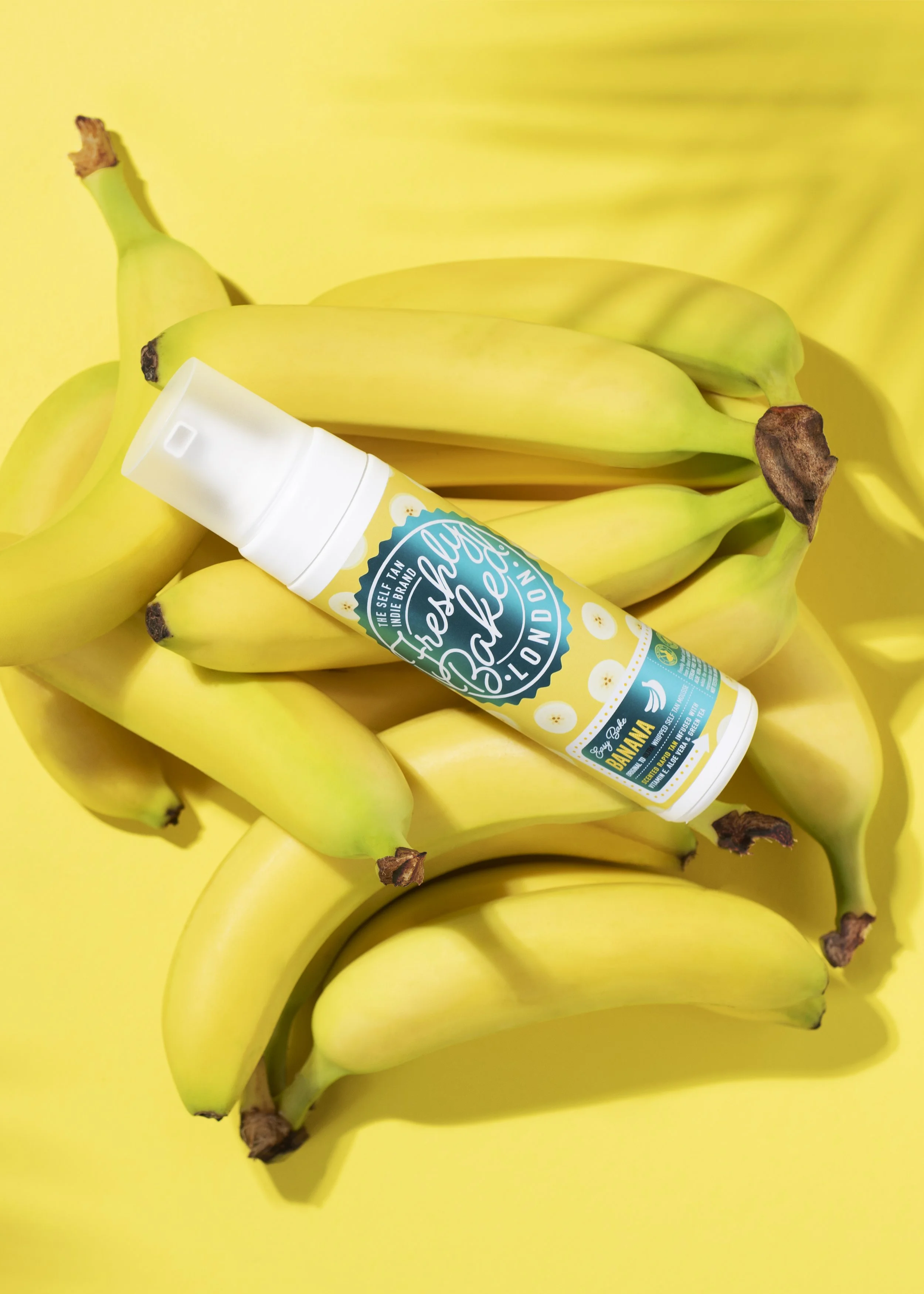 A bunch of bananas with a yellow background and a bottle of tropical-themed spray with pineapple and banana illustrations