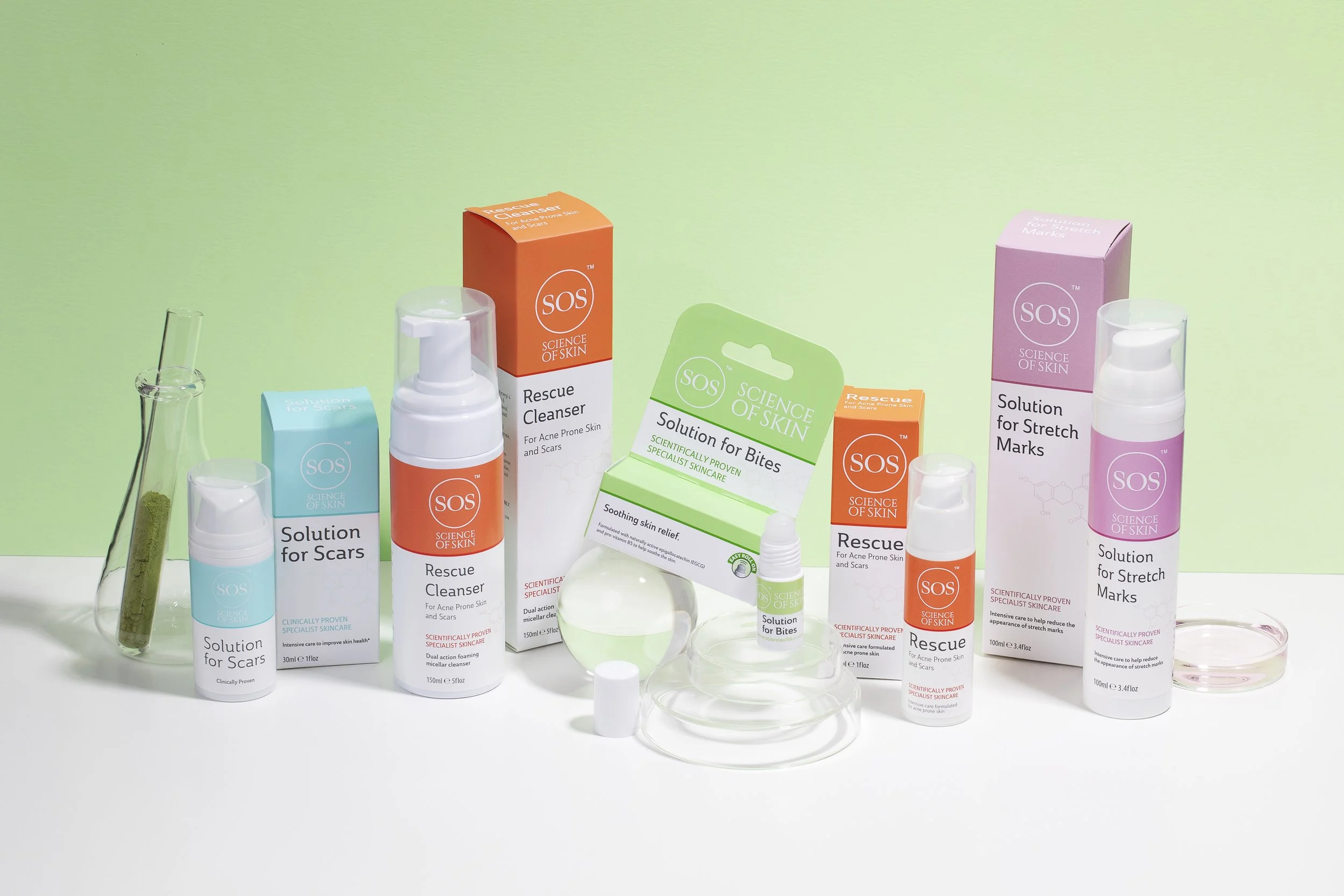 Skincare Product photography Collection of skincare products including cleansers, solutions for scars and stretch marks, in bottles and boxes with a green and orange theme, with laboratory glassware and a green background.