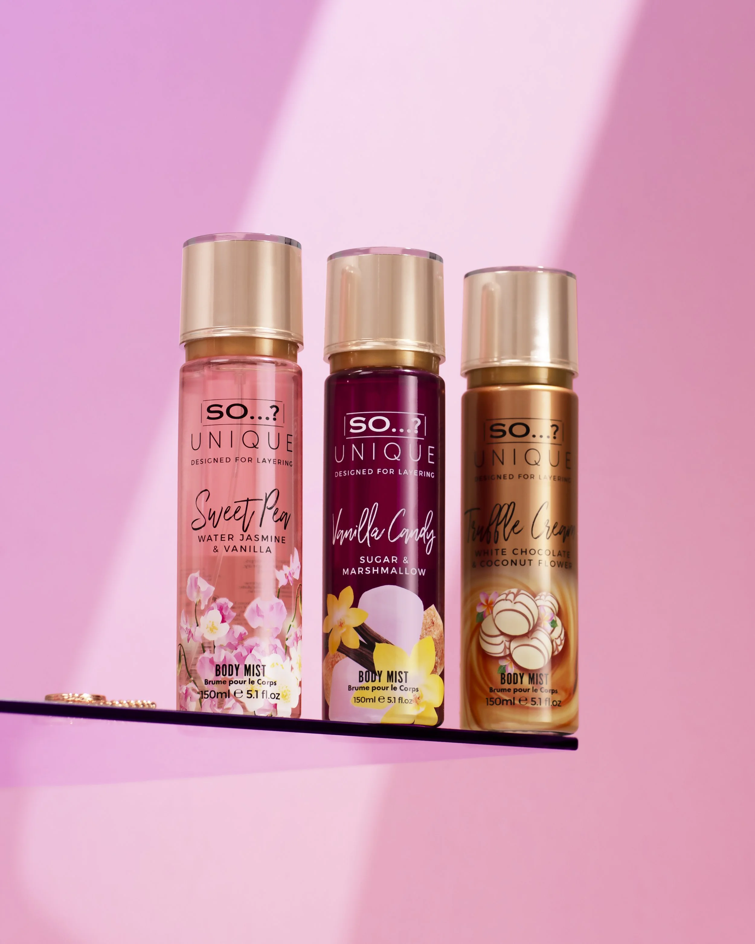 Fragrance Product photography Three bottles of body mist with pink, purple, and beige labels, labeled 'Sweet Pea,' 'Vanilla Candy,' and 'Toffee Cream' on a pink background with a reflection.