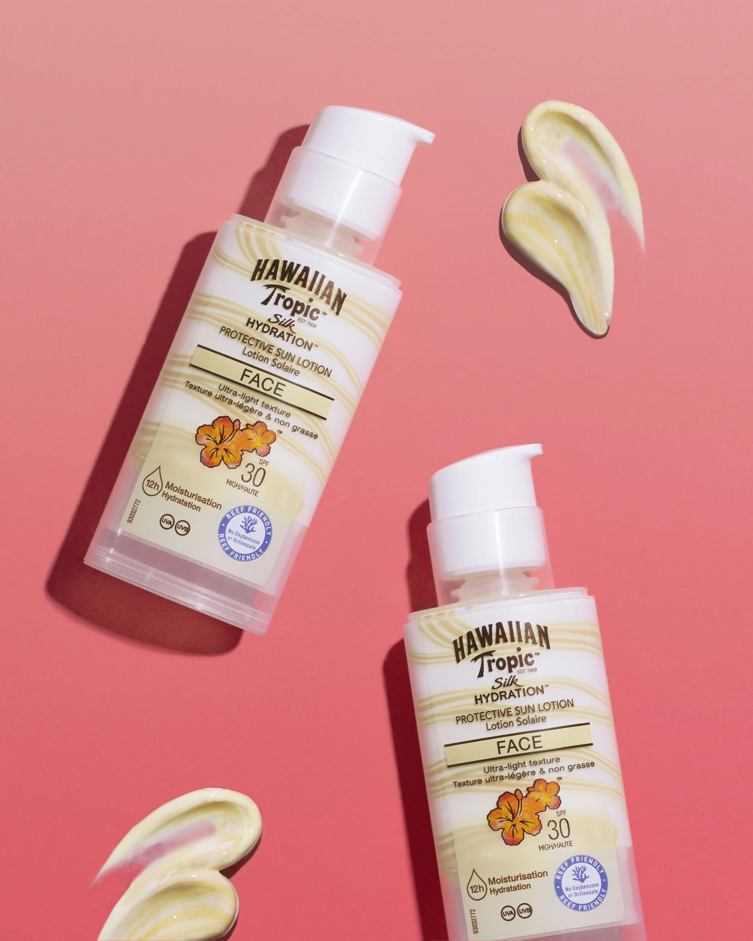 Two bottles of Hawaiian Tropic Silk Hydration protective sun lotion with SPF 30 on a pink background, with a swirl of cream and a dollop of lotion nearby.