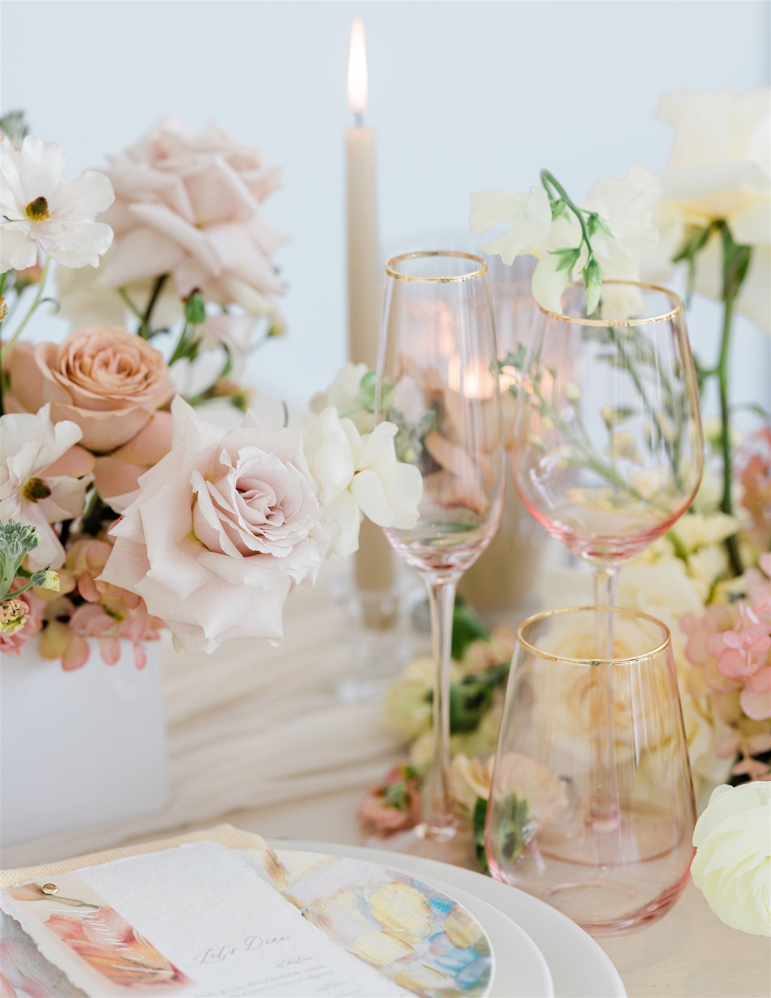 Elegant table setting with pink and white flowers, champagne flutes, and a lit candle.