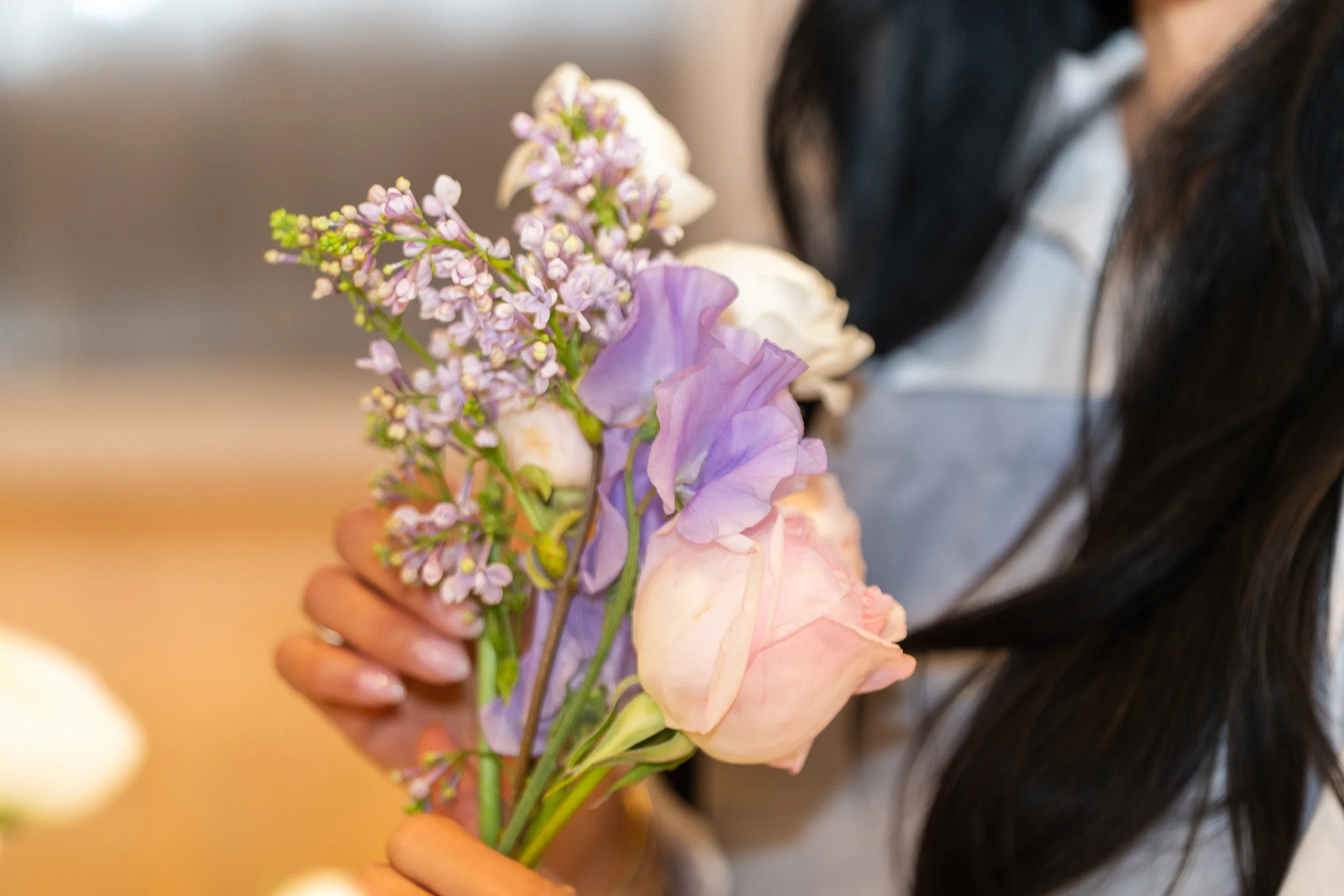 Close-up of a person holding a bouquet of pastel-colored flowers, including purple, pink, and white blossoms.