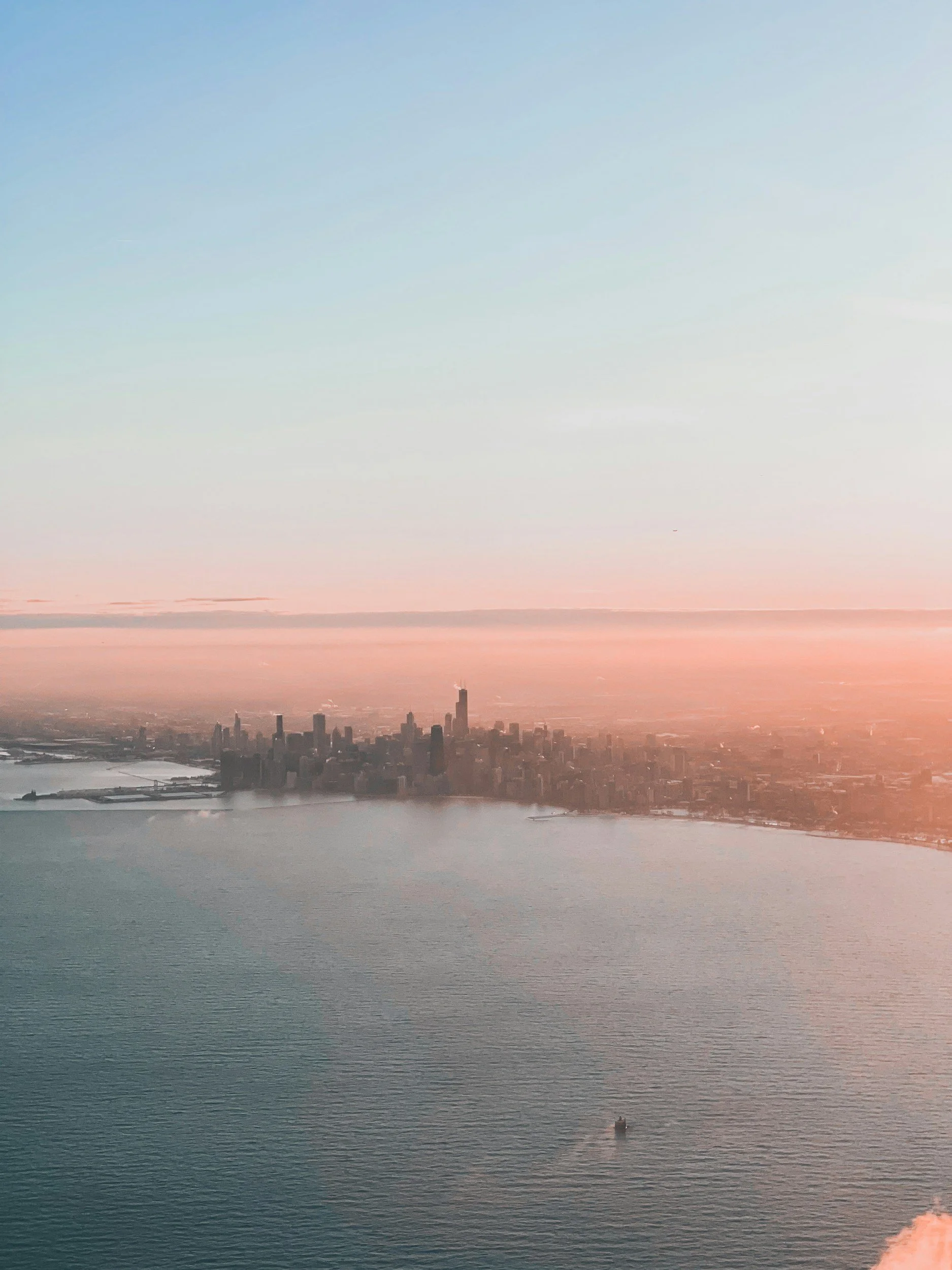 Aerial view of the Chicago skyline at sunset, with tall skyscrapers near the water and a boat on the water in the foreground.