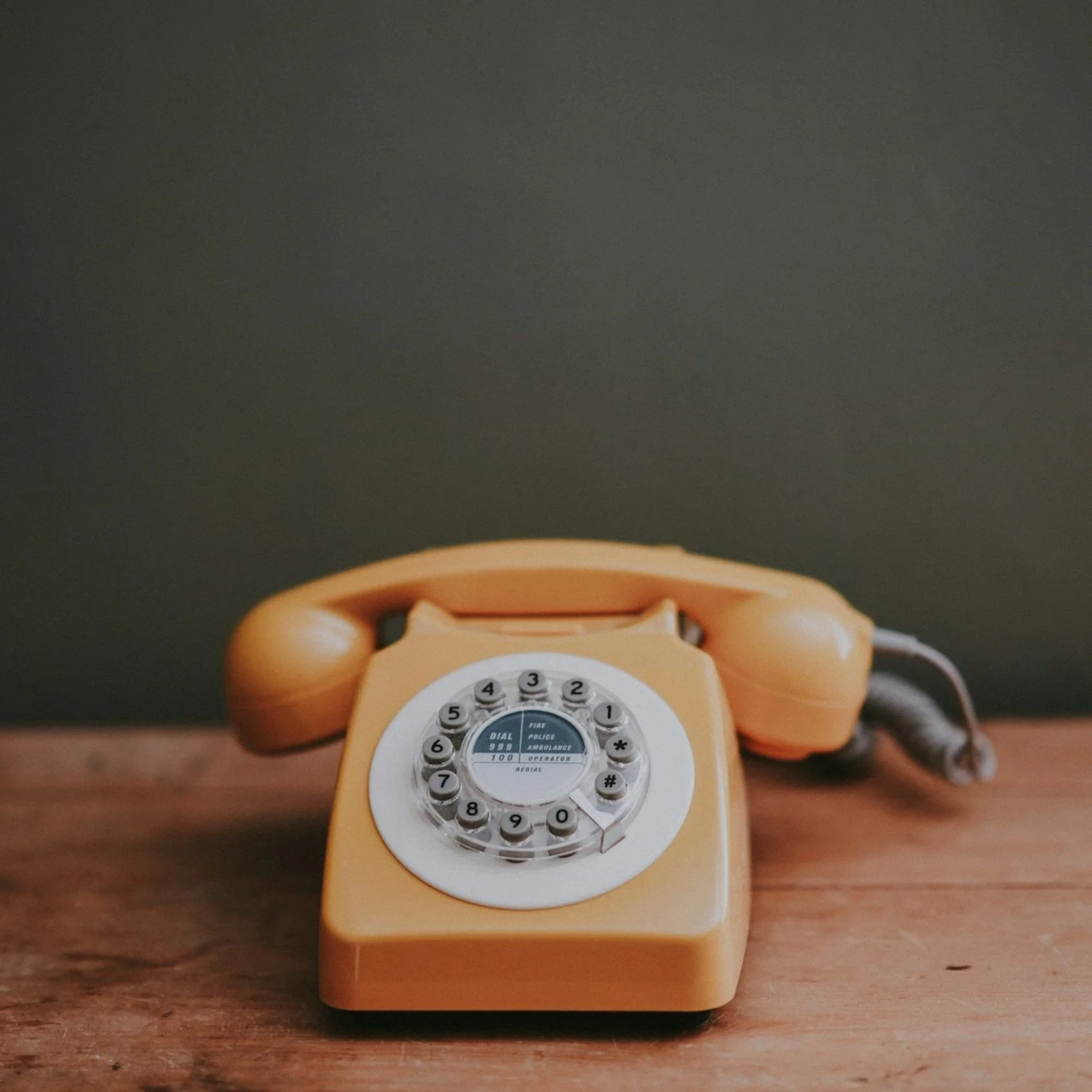 A vintage yellow rotary telephone on a wooden surface.