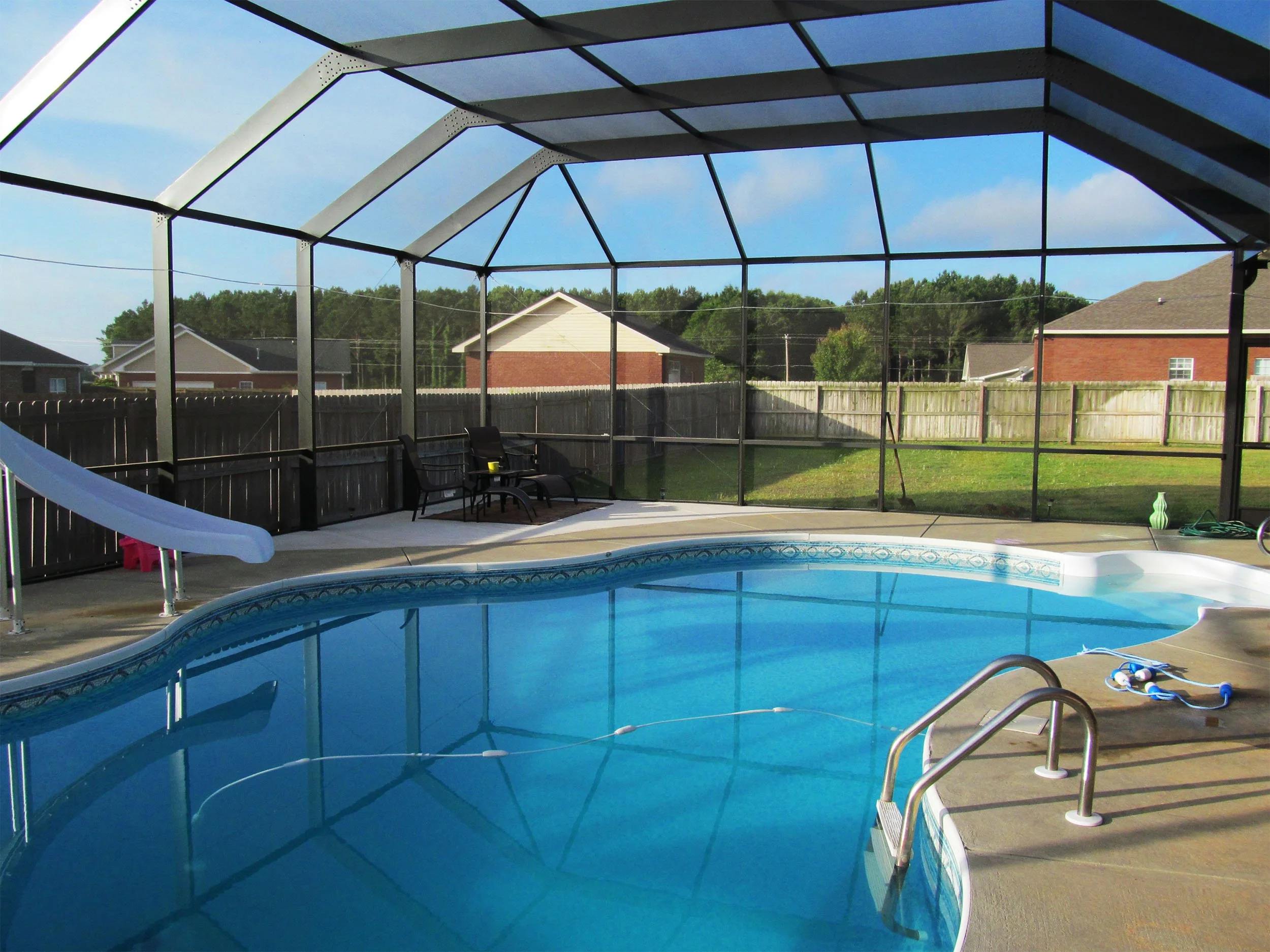 Screened pool enclosure installed around a backyard pool and patio area.