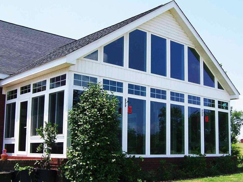 Large house with a prominent A-frame roof and extensive glass windows on the front, including a row of small rectangular windows near the roofline, surrounded by greenery and a lawn.