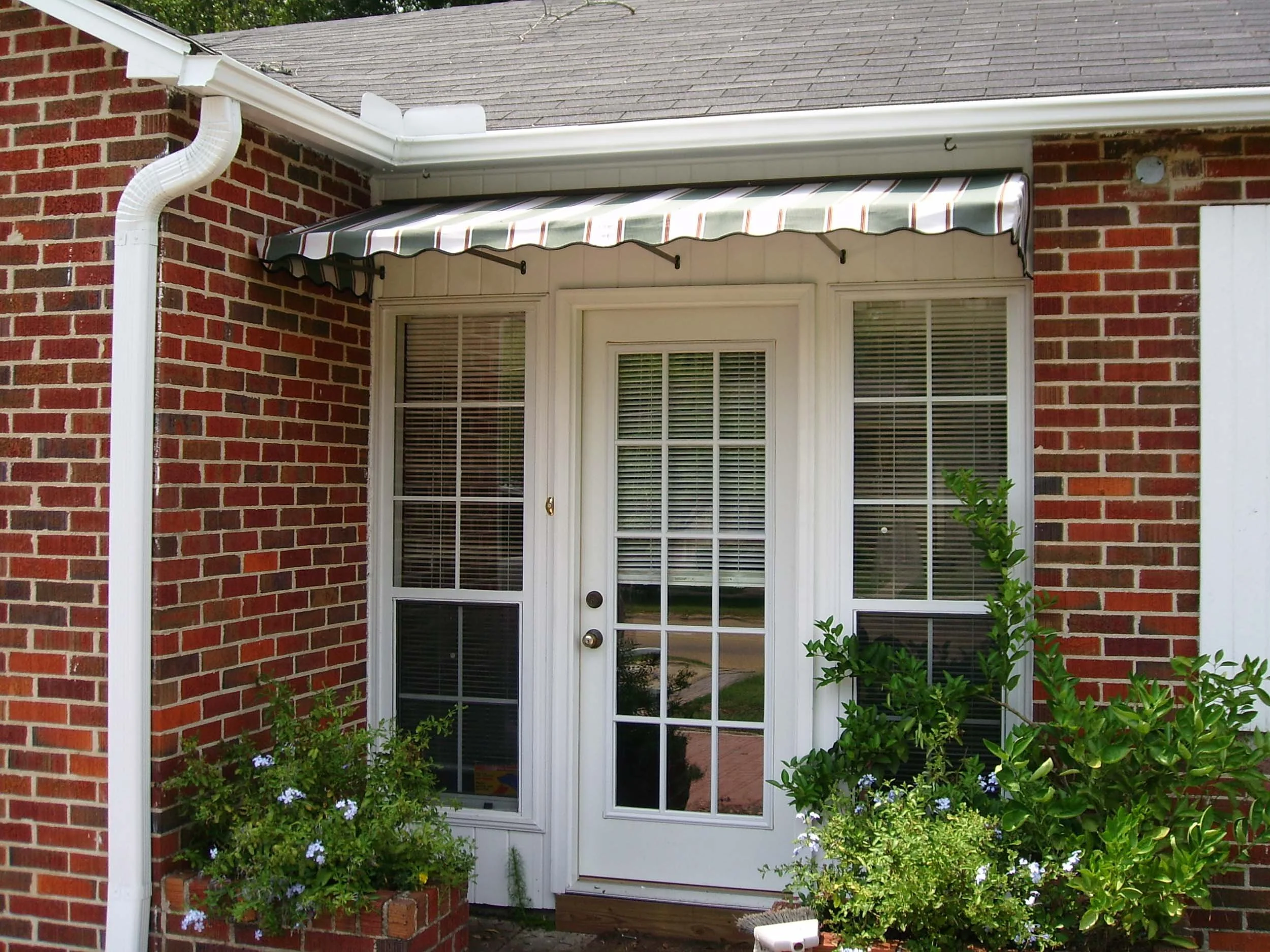 Custom window and door awning installed on a brick home for shade and curb appeal.