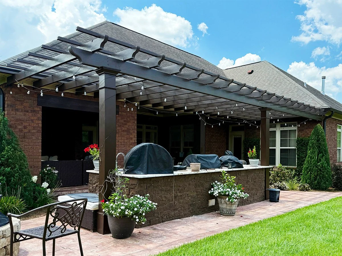 Backyard patio with a covered grill area, potted plants with flowers, outdoor furniture, and string lights