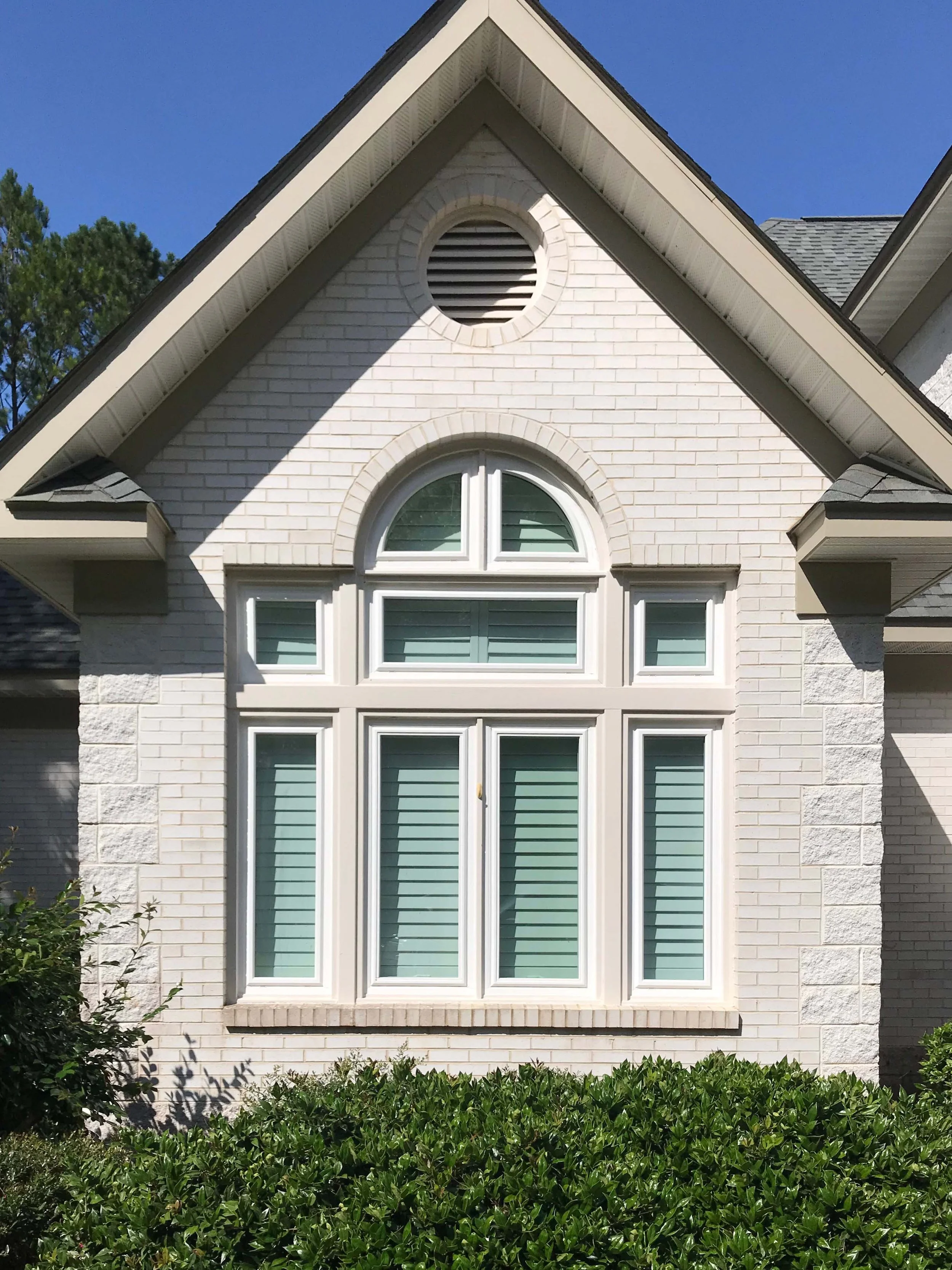 Replacement windows with specialty-shaped windows on a brick home exterior.