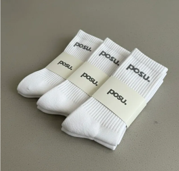 Three pairs of white socks with brand labels, neatly folded and stacked on a gray surface.