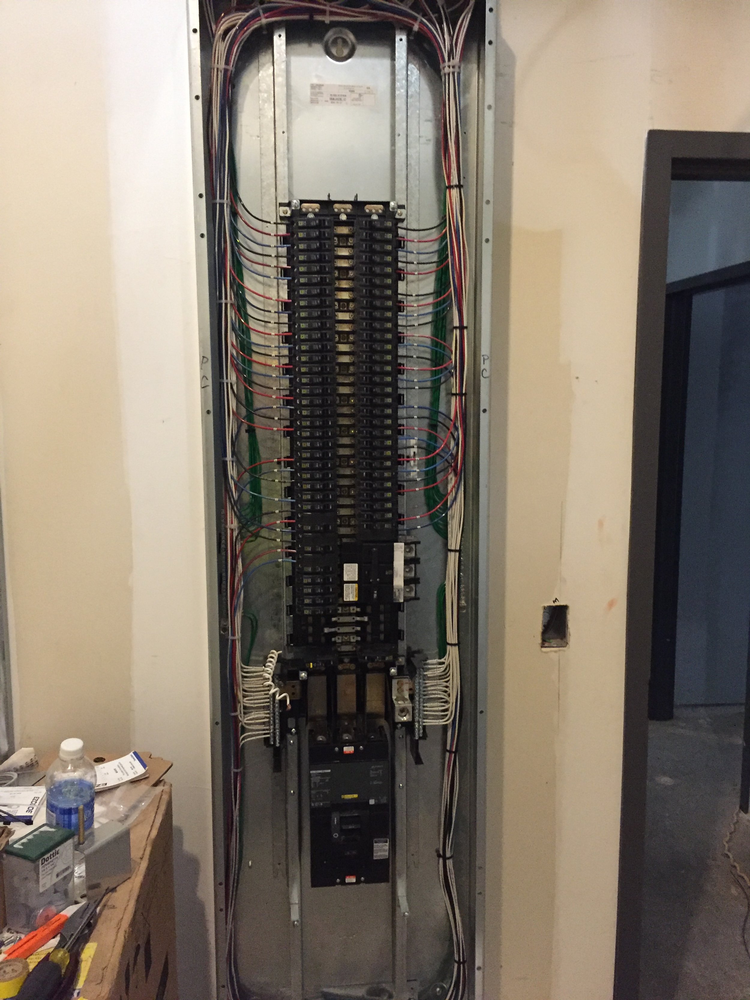 Electrical panel with circuit breakers and wiring inside a wall.