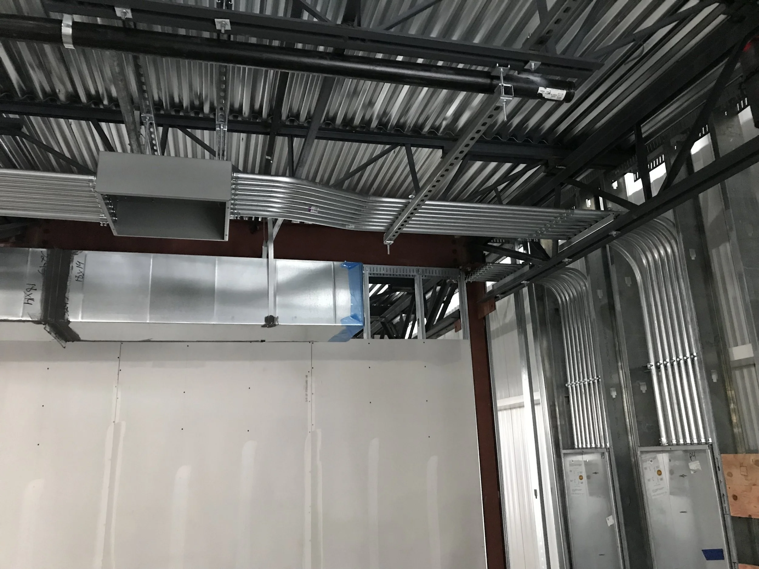 Interior view of a building under construction or renovation, featuring metal framing, electrical conduit pipes, and a partly finished wall.