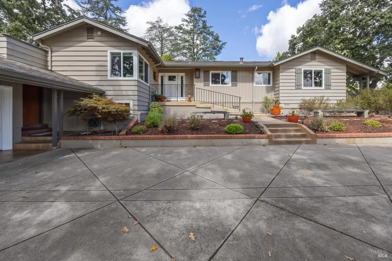 Front view of a house with a concrete driveway, landscaped yard, and stairs leading up to the porch.