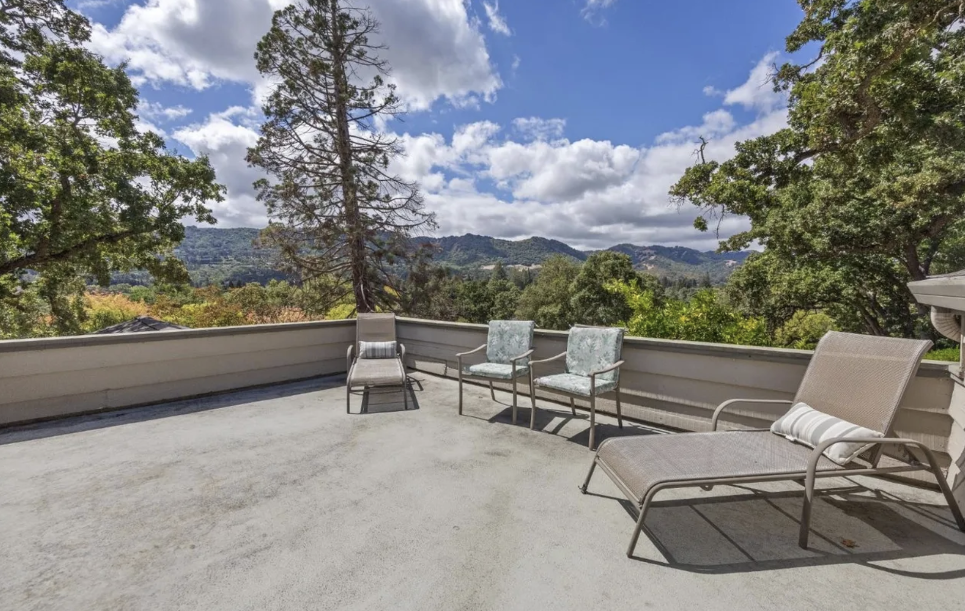 Outdoor balcony with lounge chairs and mountain view under partly cloudy sky.