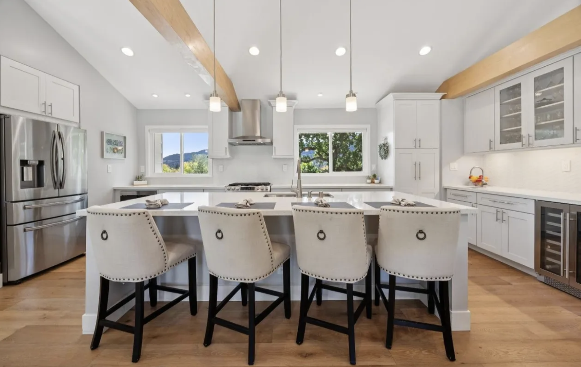 Modern kitchen with white cabinets, large island with seating, stainless steel appliances, and wooden ceiling beams