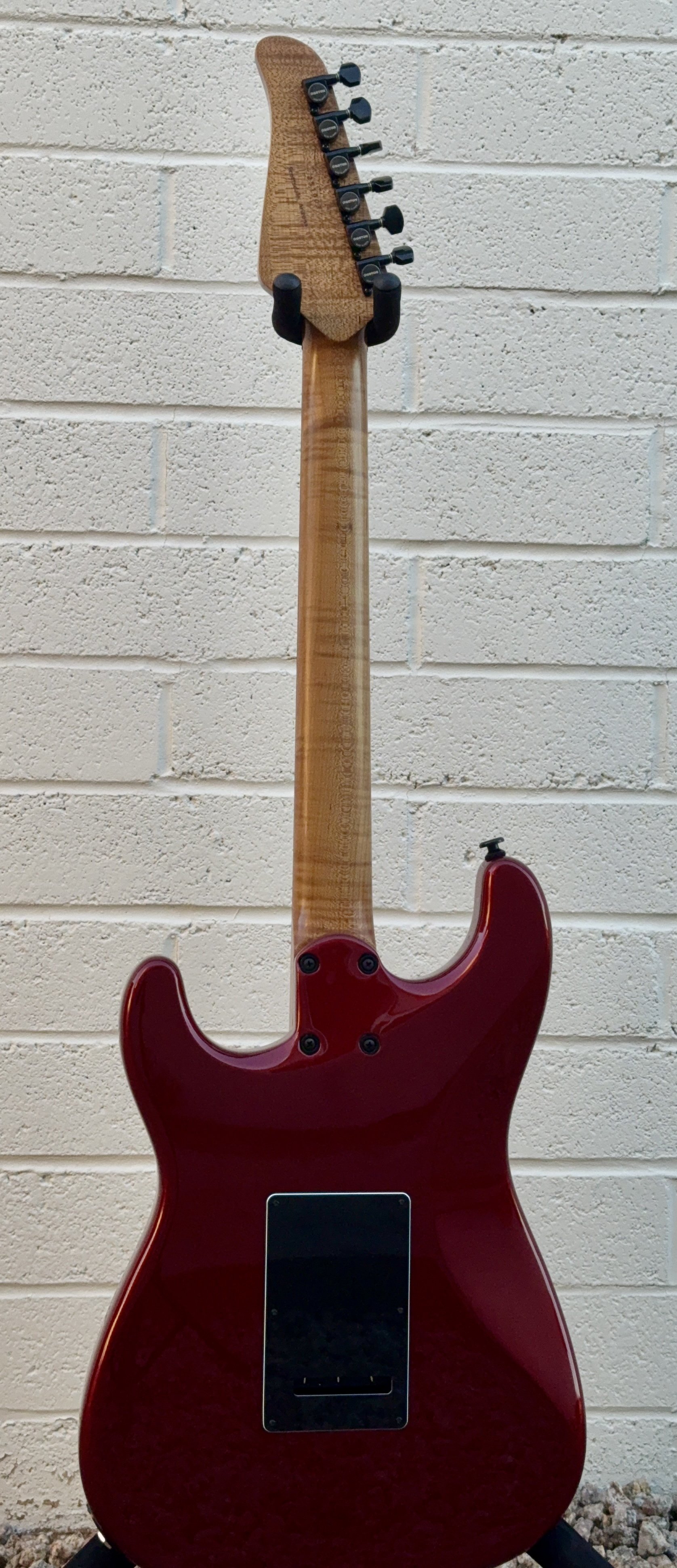 Red electric guitar with a natural wood neck, mounted on a wall against a white brick background.