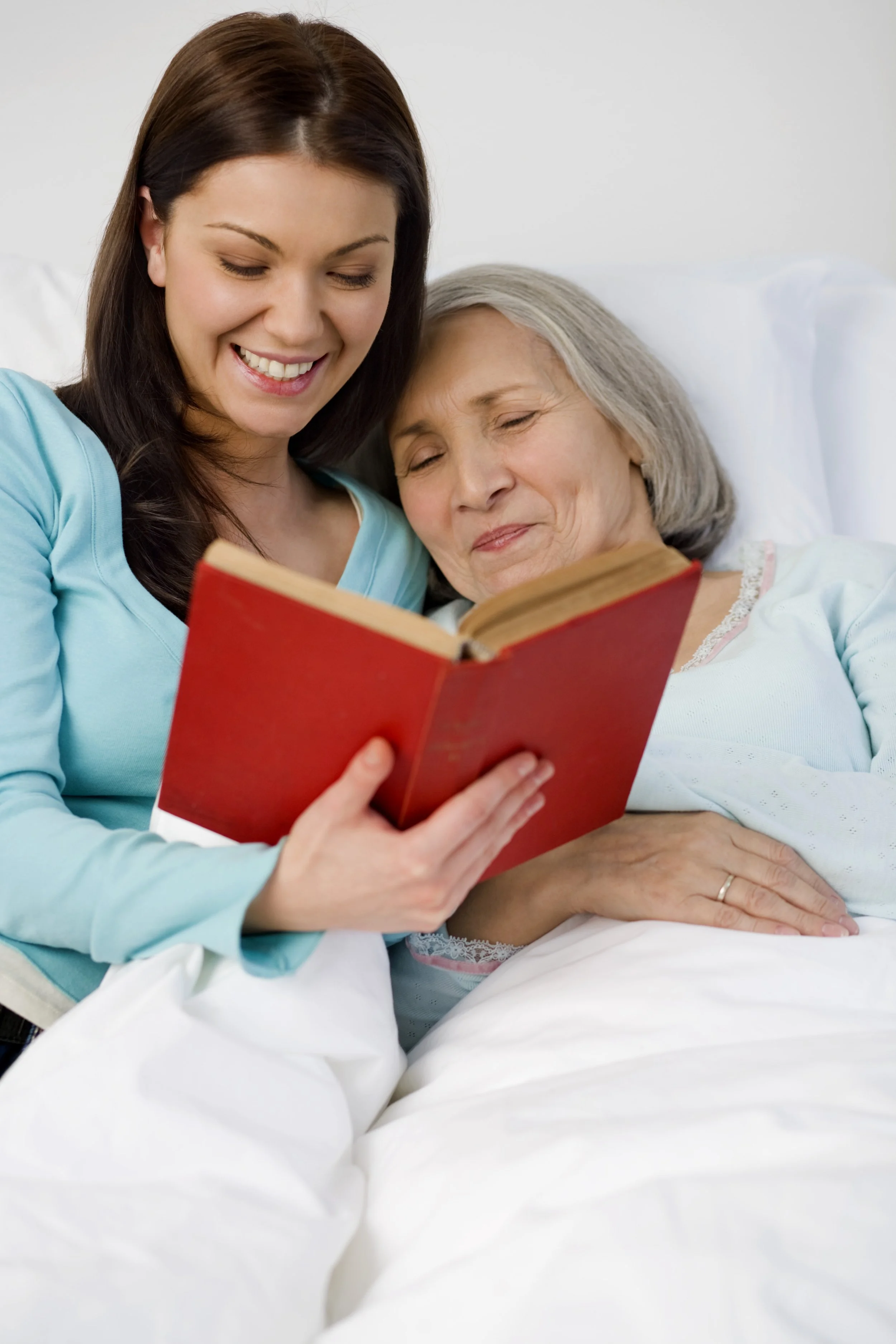 A young woman in a hospital bed sharing a joyful moment with an elderly woman, both holding a red book.