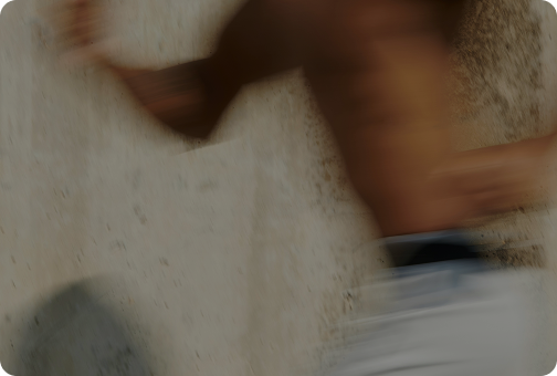 Blurred image of a person running or jumping, with a concrete or sandy background.