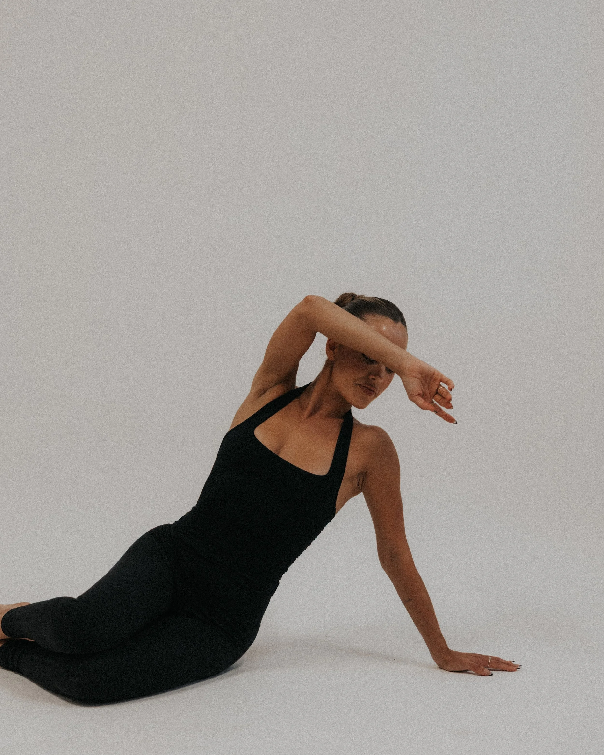 A woman performing a yoga pose on a plain white background, wearing a black tank top and black pants.