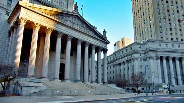 The New York County Courthouse in New York City with its neoclassical architecture, tall columns, and steps leading up to the entrance, under a clear blue sky.