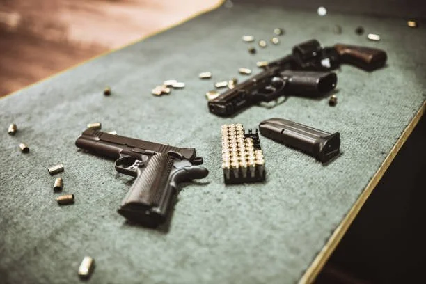 Two handguns, a magazine, bullets, and shotgun shells on a green felt table.