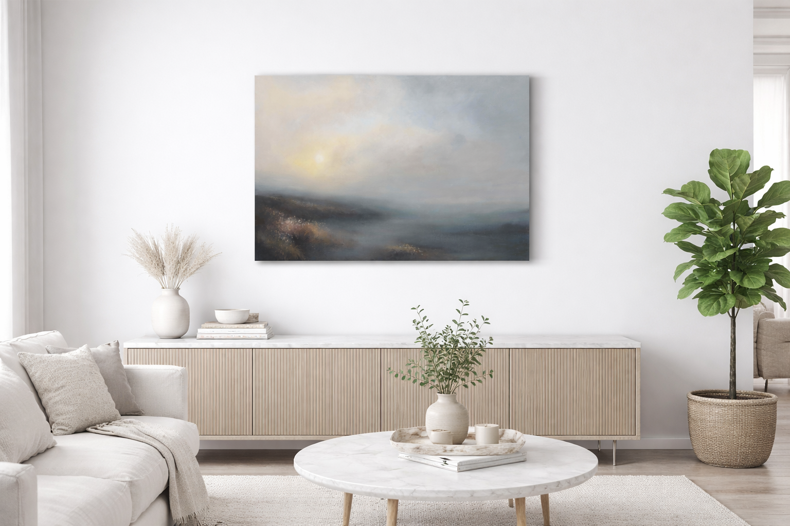 Minimalist living room with white sofa, beige cushions, and a round marble coffee table with a vase and books. White sideboard with decorative items and a large green potted plant. Abstract landscape painting on the wall.