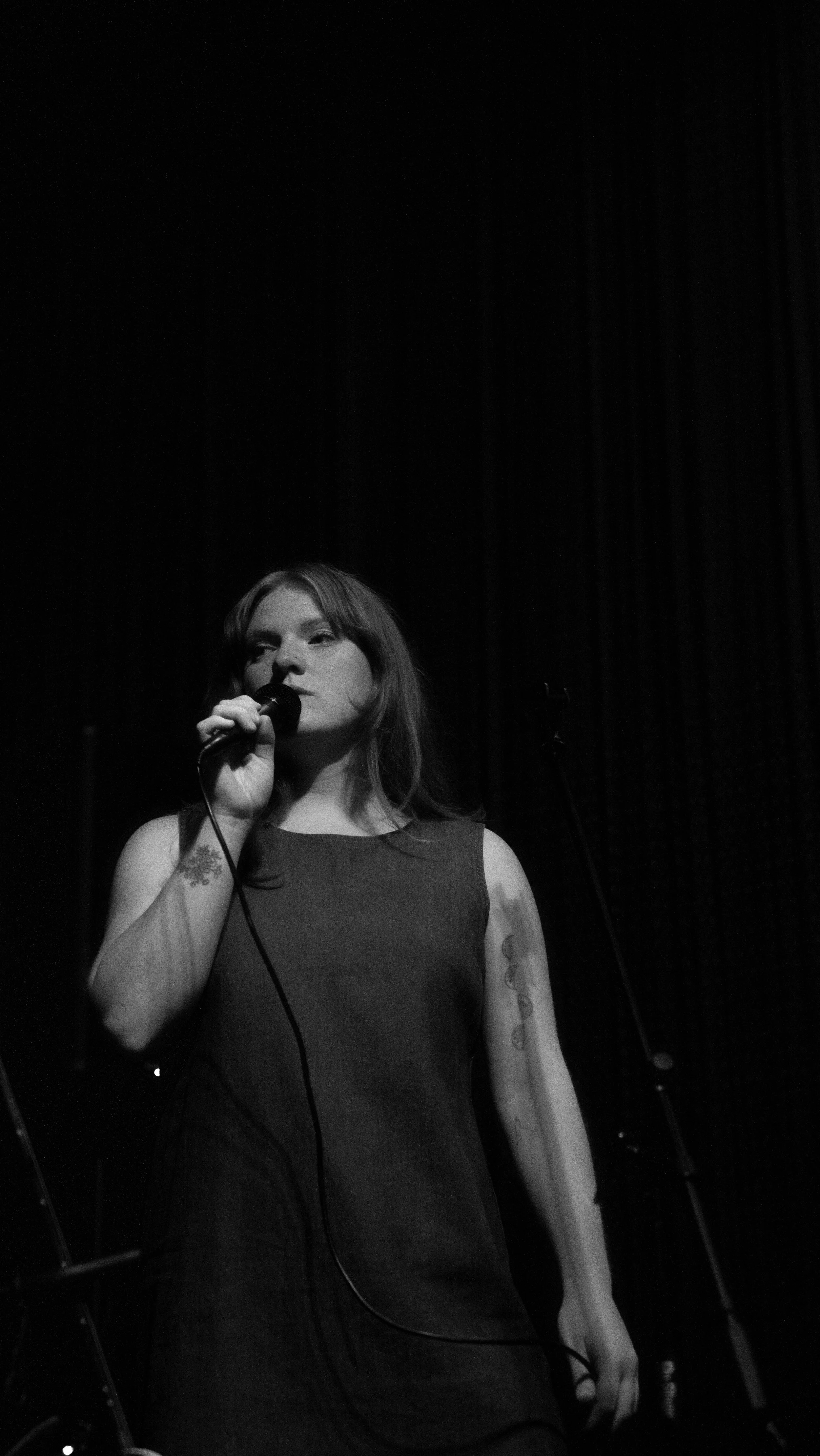 A woman singing into a microphone on stage with a dark background.