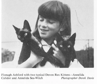 A young woman holding two black cats with large eyes, one in each arm, in black and white.
