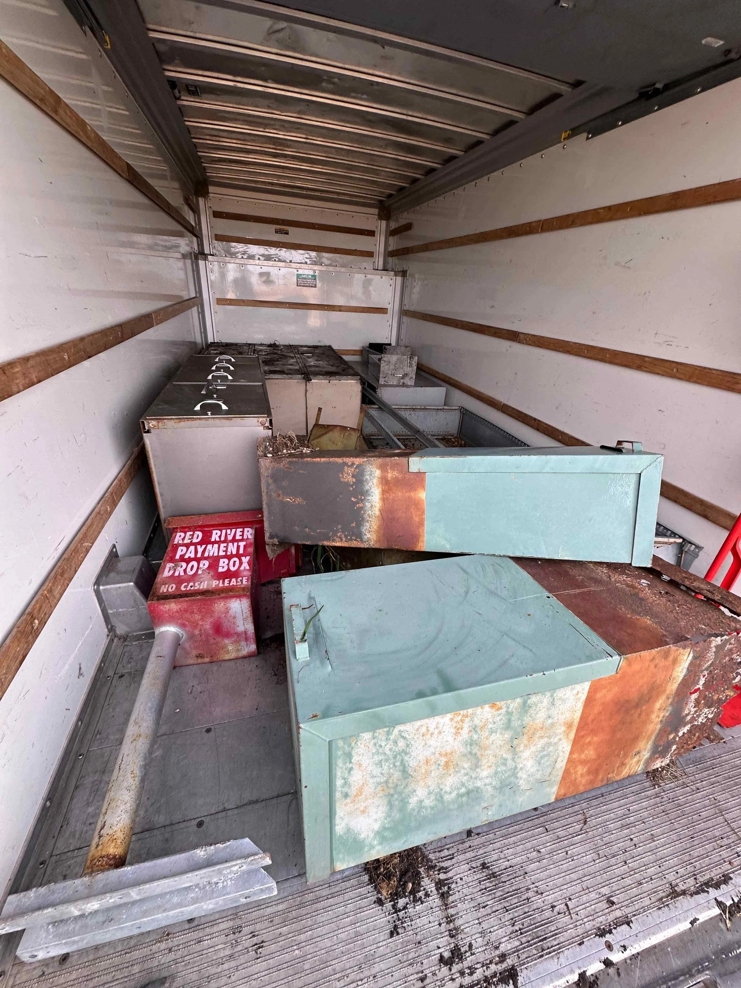Inside an empty, rusty food truck kitchen with kitchen appliances and a red payment drop box labeled "RED RIVER PAYMENT DROP BOX NO CASH PLEASE."
