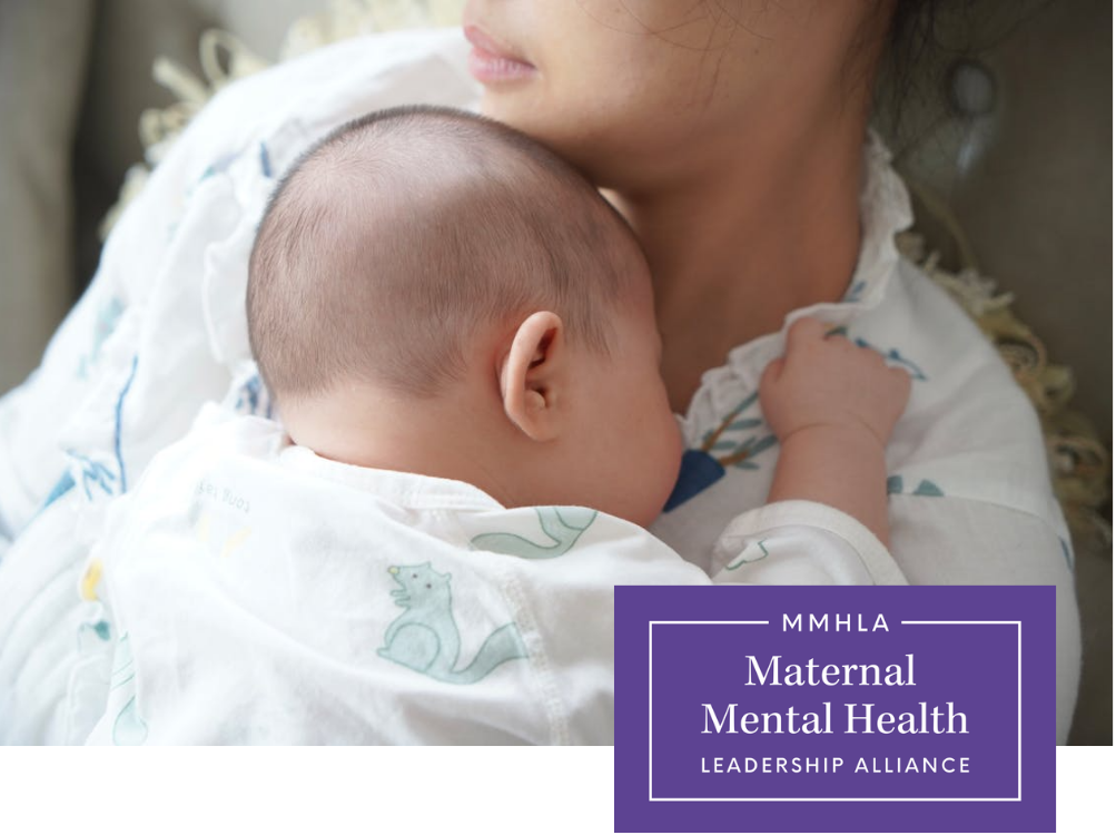 A woman holding a sleeping baby with a bald head and wearing a white onesie with dinosaur prints, resting against her shoulder.