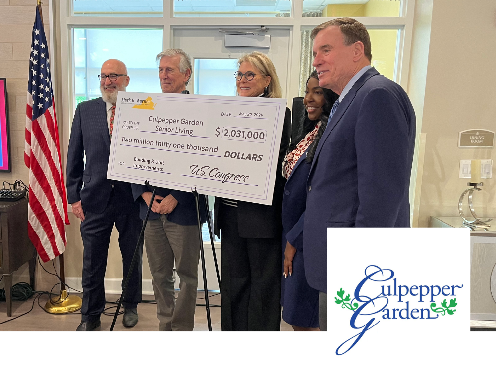 A group of five people, three men and two women, standing together indoors, holding a large ceremonial check for over two million dollars made out to Culpeper Garden Senior Living, dated May 20, 2024, with a U.S. Congress signature. There is an American flag and a window in the background, and the Culpeper Garden logo is visible in the corner.