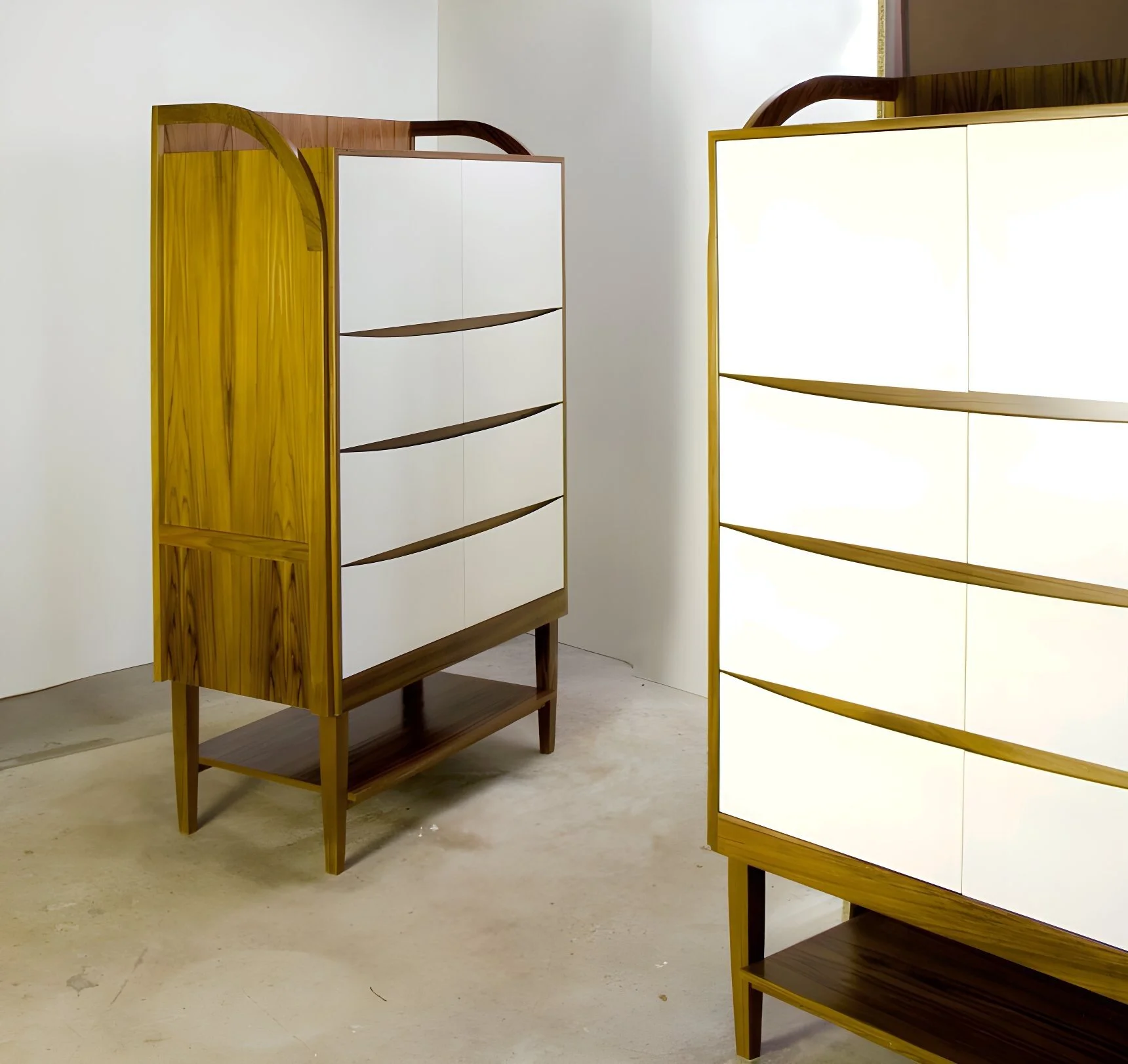 Two modern wooden dressers with white drawers and arched tops, placed on a plain concrete floor in a minimalist room.