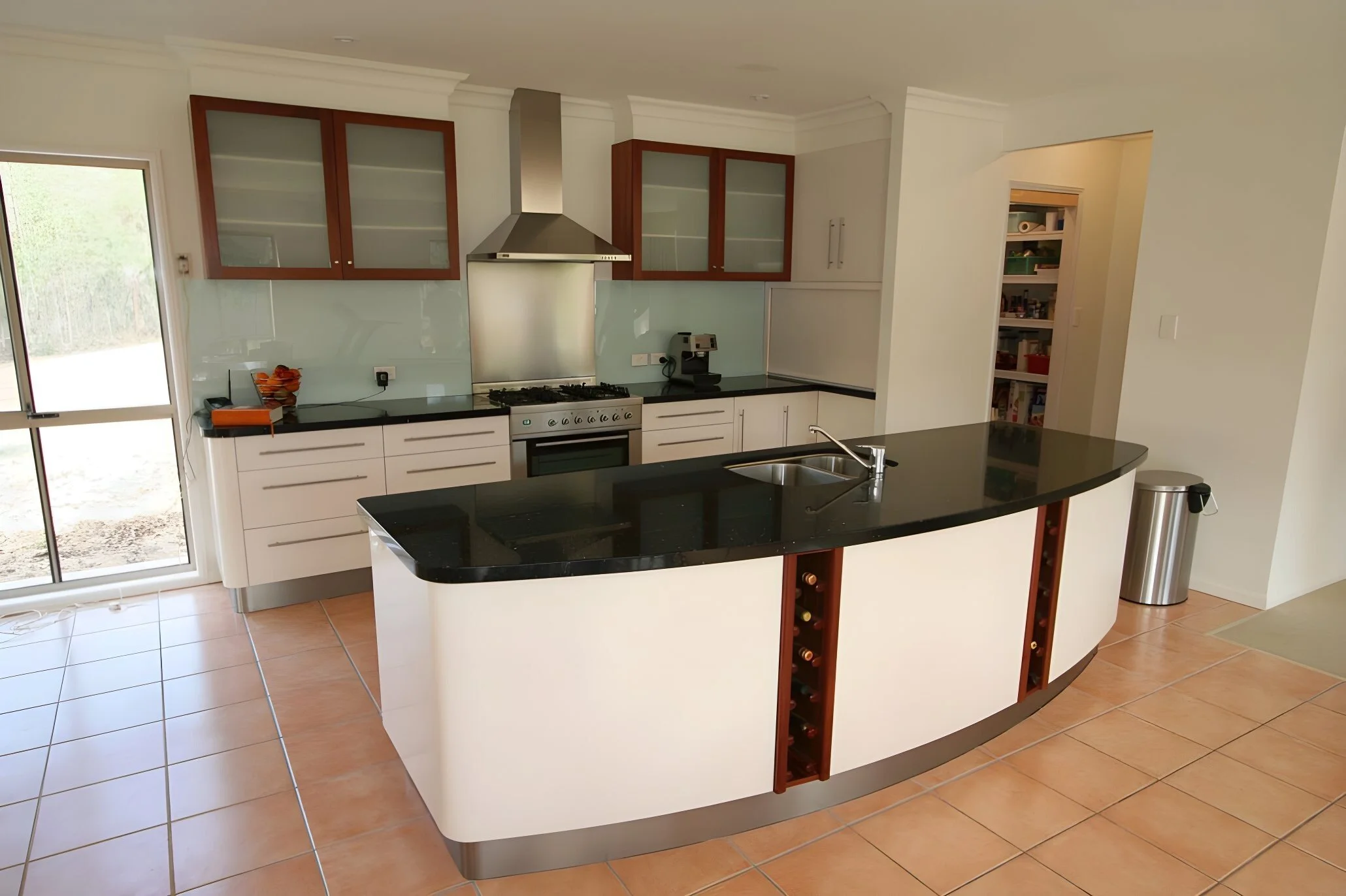 Modern kitchen with white cabinets, black countertops, stainless steel appliances, and a curved island with a sink and wine rack