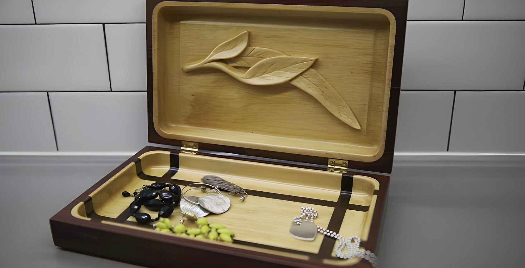 Open jewelry box containing various jewelry pieces on a countertop with white tile background.