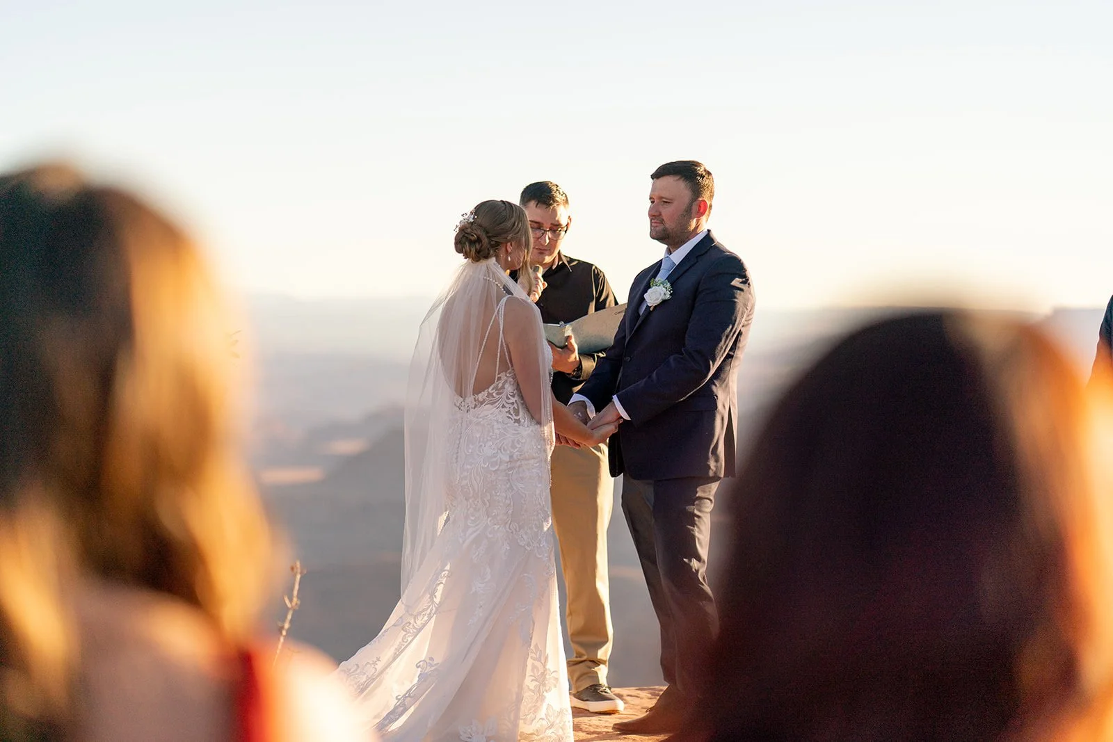 A couple getting married outdoors at sunset with people in the foreground watching the ceremony