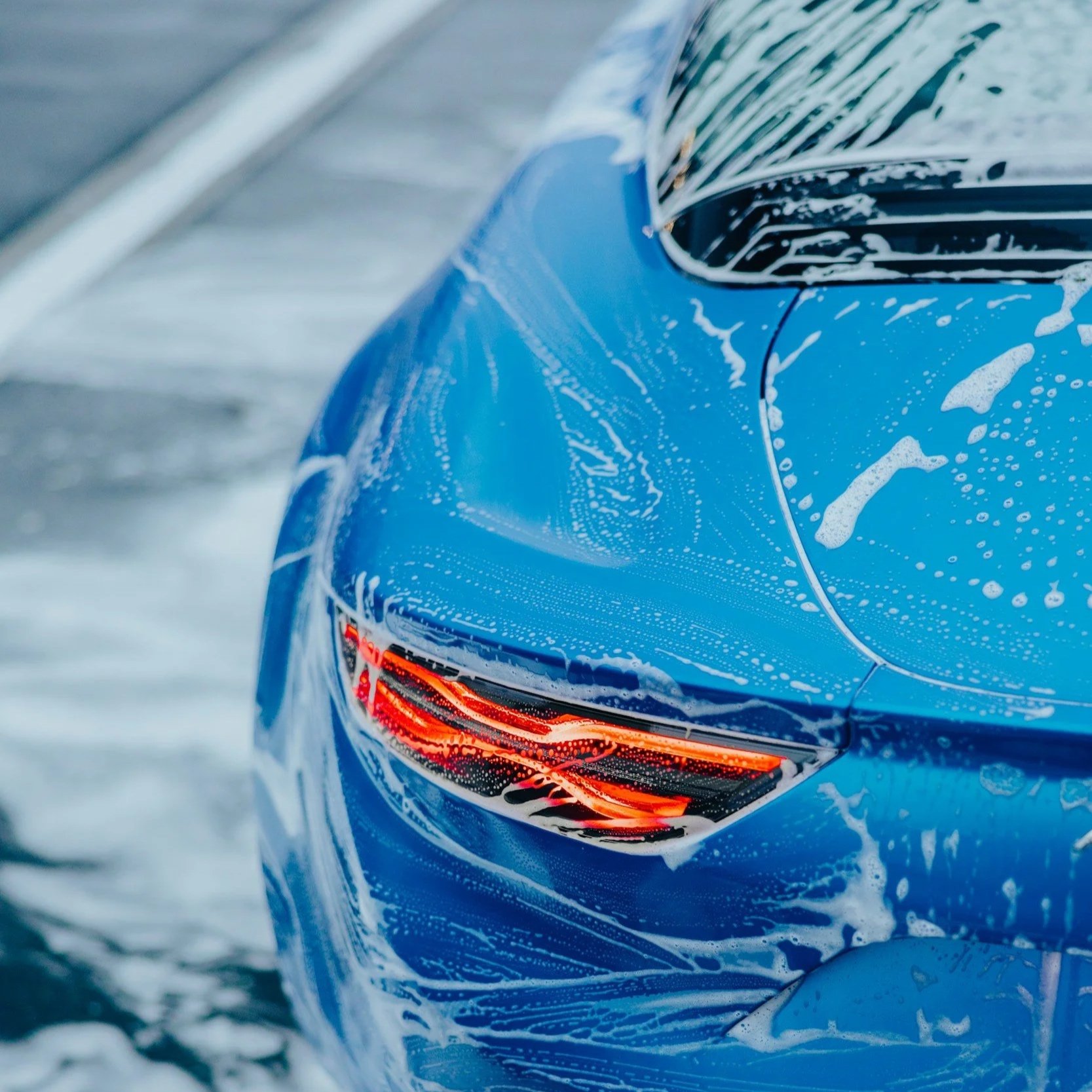 Close-up of a blue car's rear, covered in soap suds, with the brake light on.