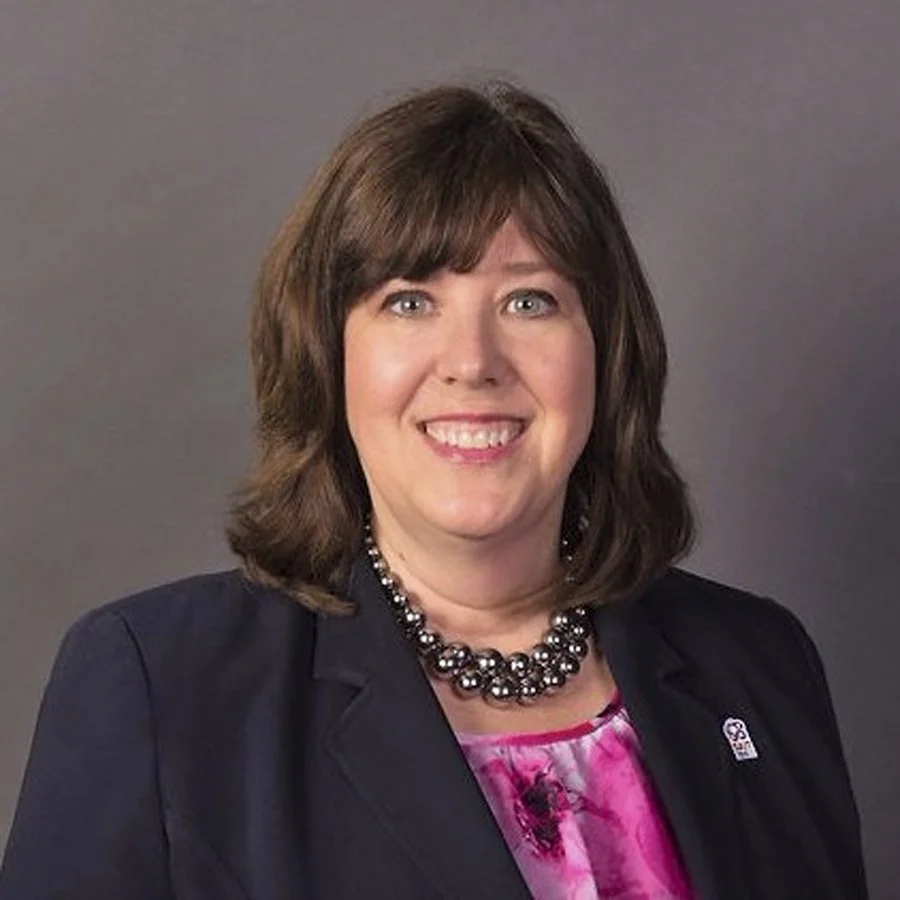 A woman with shoulder-length brown hair, wearing a black blazer, a pink and purple patterned blouse, and a large beaded necklace, smiling at the camera against a gray background. Heather Magotiaux

VP, External Relations, SAIT