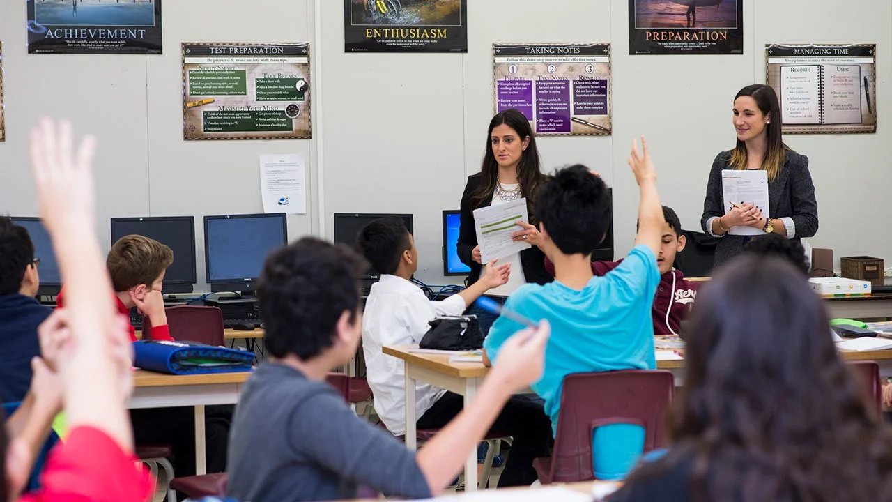 Instructors leading a classroom discussion with students raising their hands during a JA (Junior Achievement) Southern Alberta program