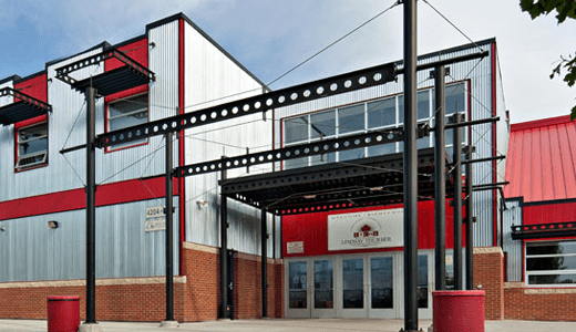 Exterior of a sports complex or gym with a red and white color scheme, metal siding, and a large entrance under a black metal awning.