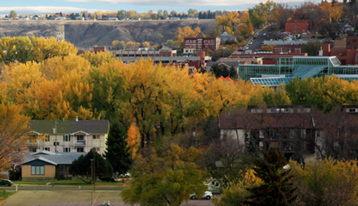 A cityscape with colorful fall trees, houses, and buildings on rolling hills in the background.