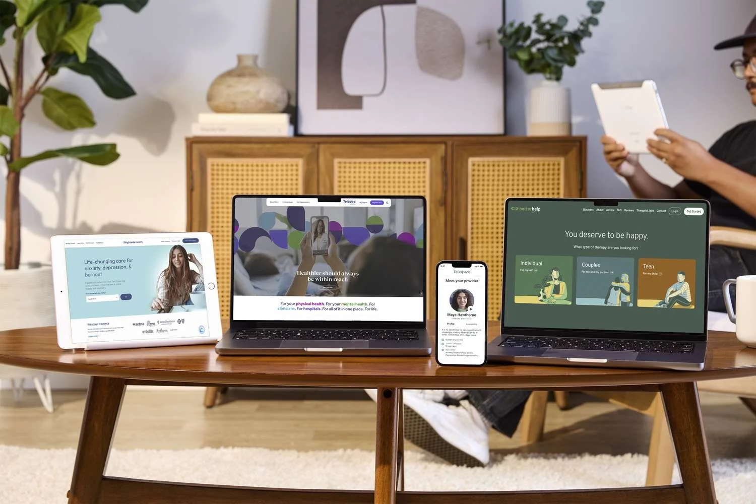 A wooden table with various digital devices displaying health and wellness websites, including a tablet, a laptop, and a smartphone. Home health virtual consultation.