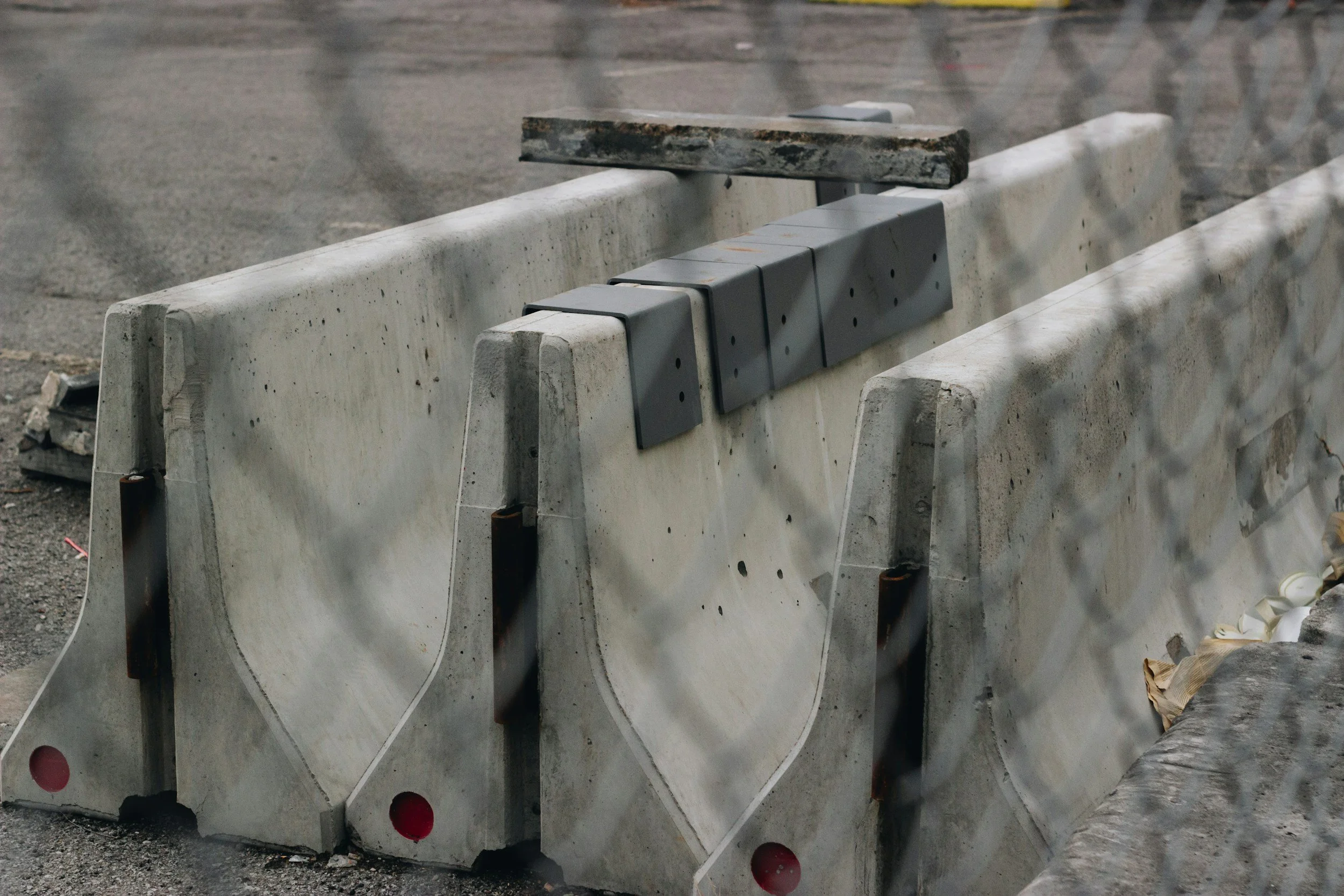 Concrete barriers with mounted black rubber strips and a rusted metal beam on top, placed along a construction site or roadwork area.