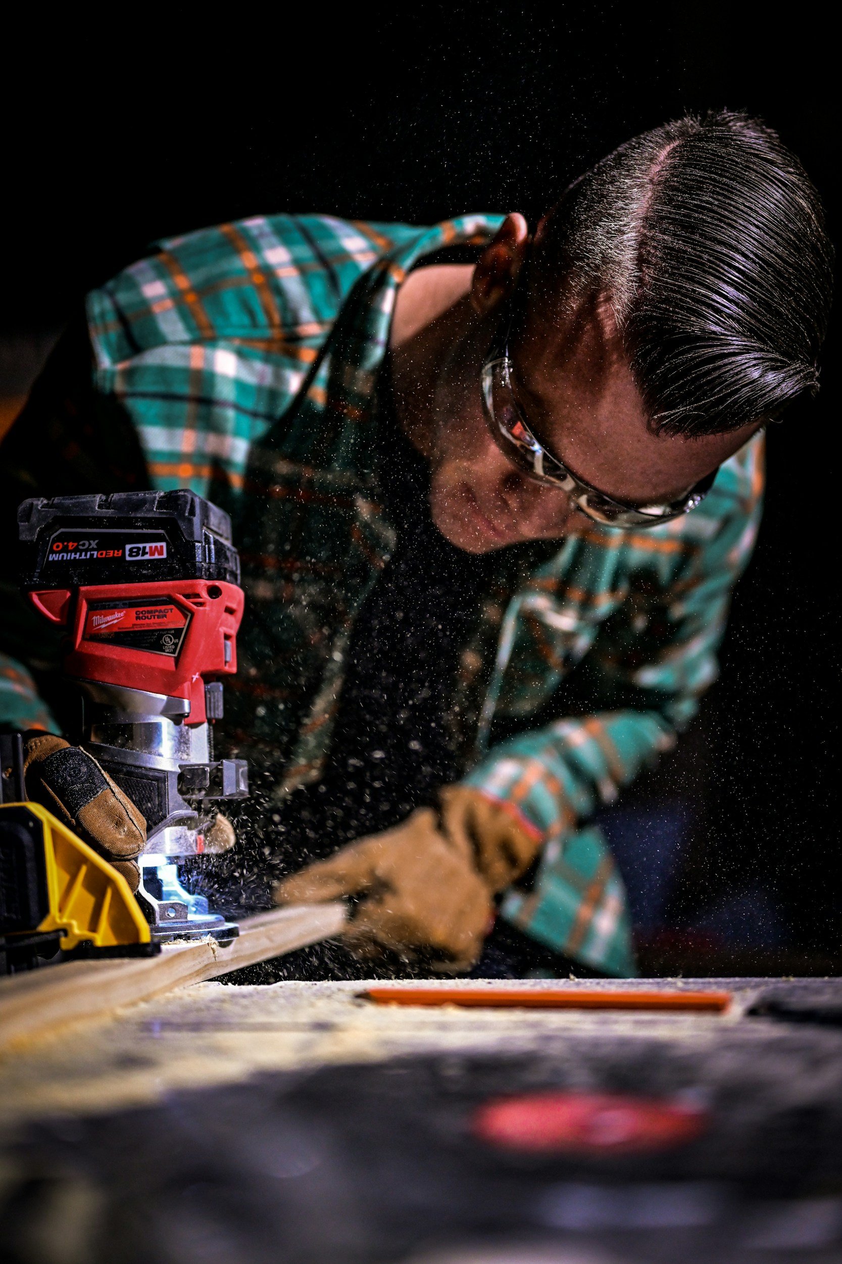 A person cutting wood with a power saw, wearing safety goggles and gloves, with wood dust in the air.