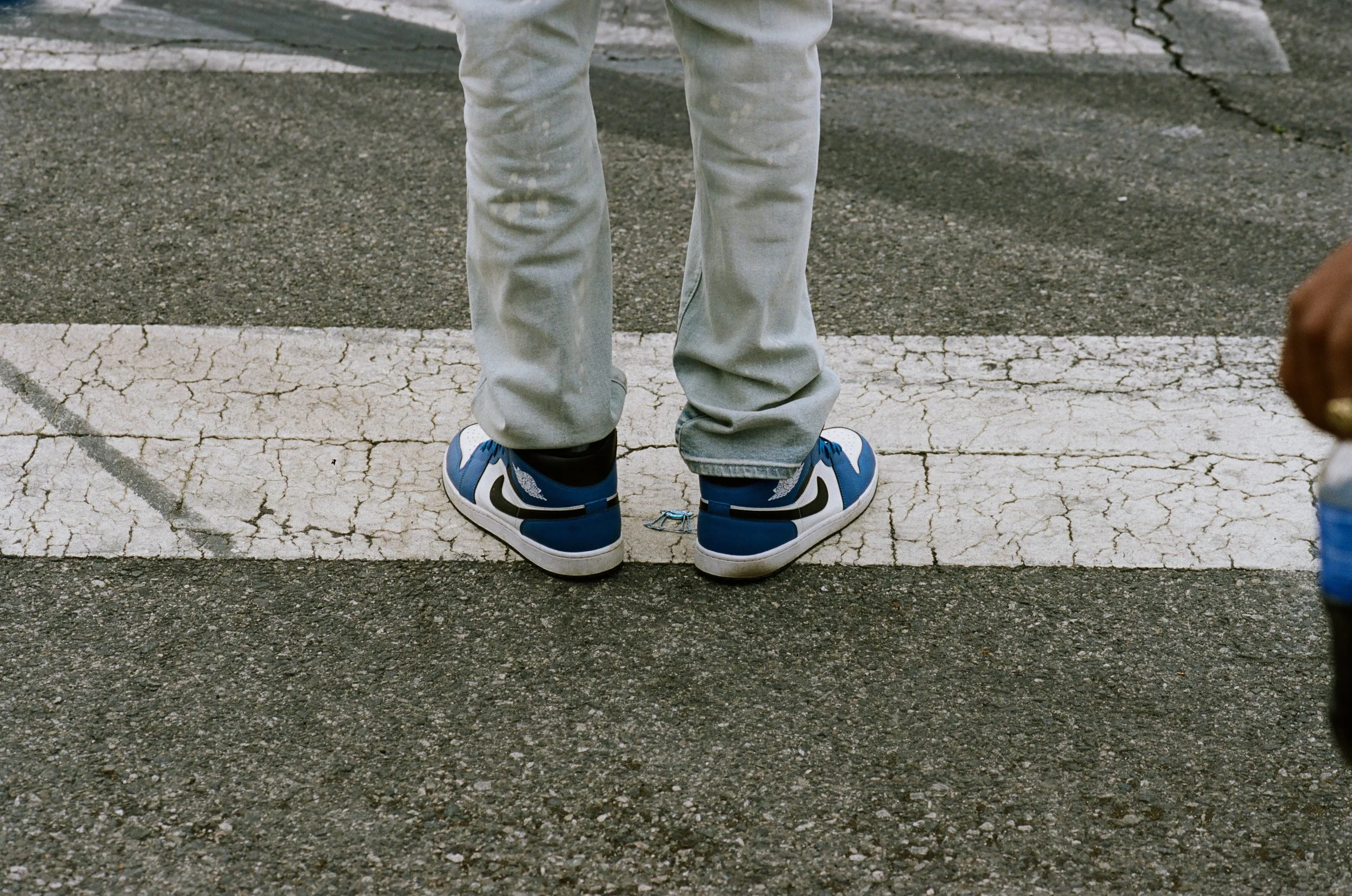 Person standing in a parking lot wearing gray pants and blue and white sneakers.